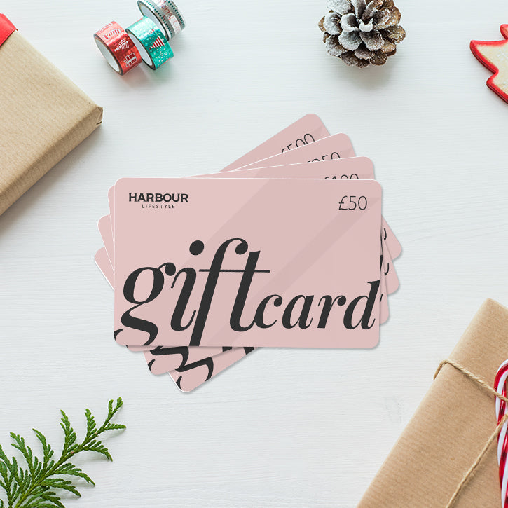 Gift cards with "Harbour Lifestyle £50" on a festive background of wrapped gifts, pinecones, and greenery.