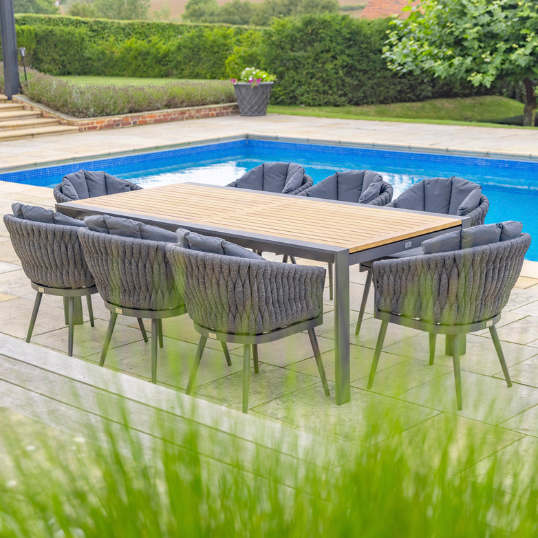 The Palma 8 Seat Rope Extending Teak Dining Set in Grey, featuring a teak table and eight cushioned chairs by the pool, surrounded by lush greenery, epitomizes the Harbour Lifestyle.