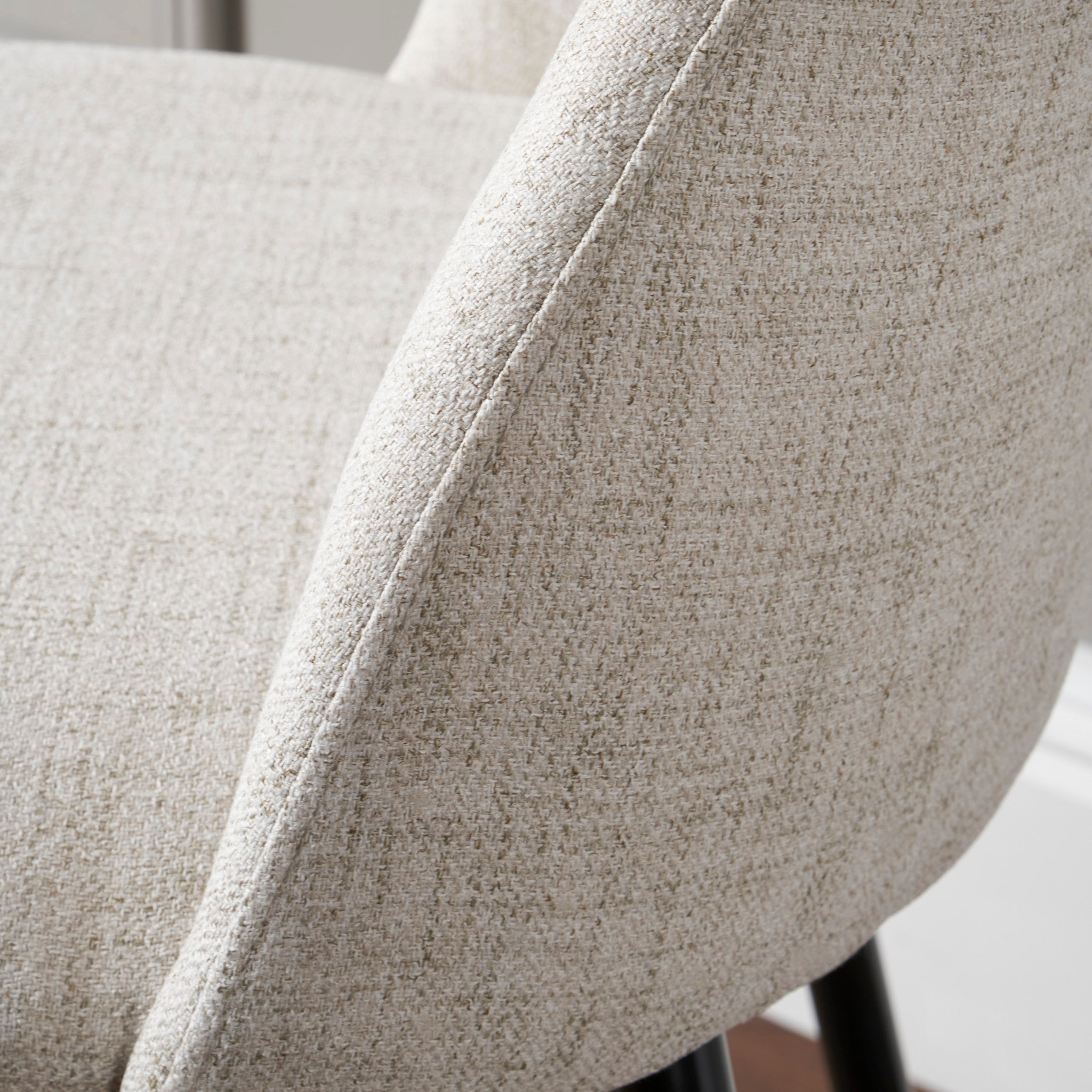 Close-up of the Turi Pebble Linen Mix and Black Metal Bar Stool, featuring its light gray upholstered seat with textured fabric, showcasing part of the backrest and embodying a contemporary modern style.