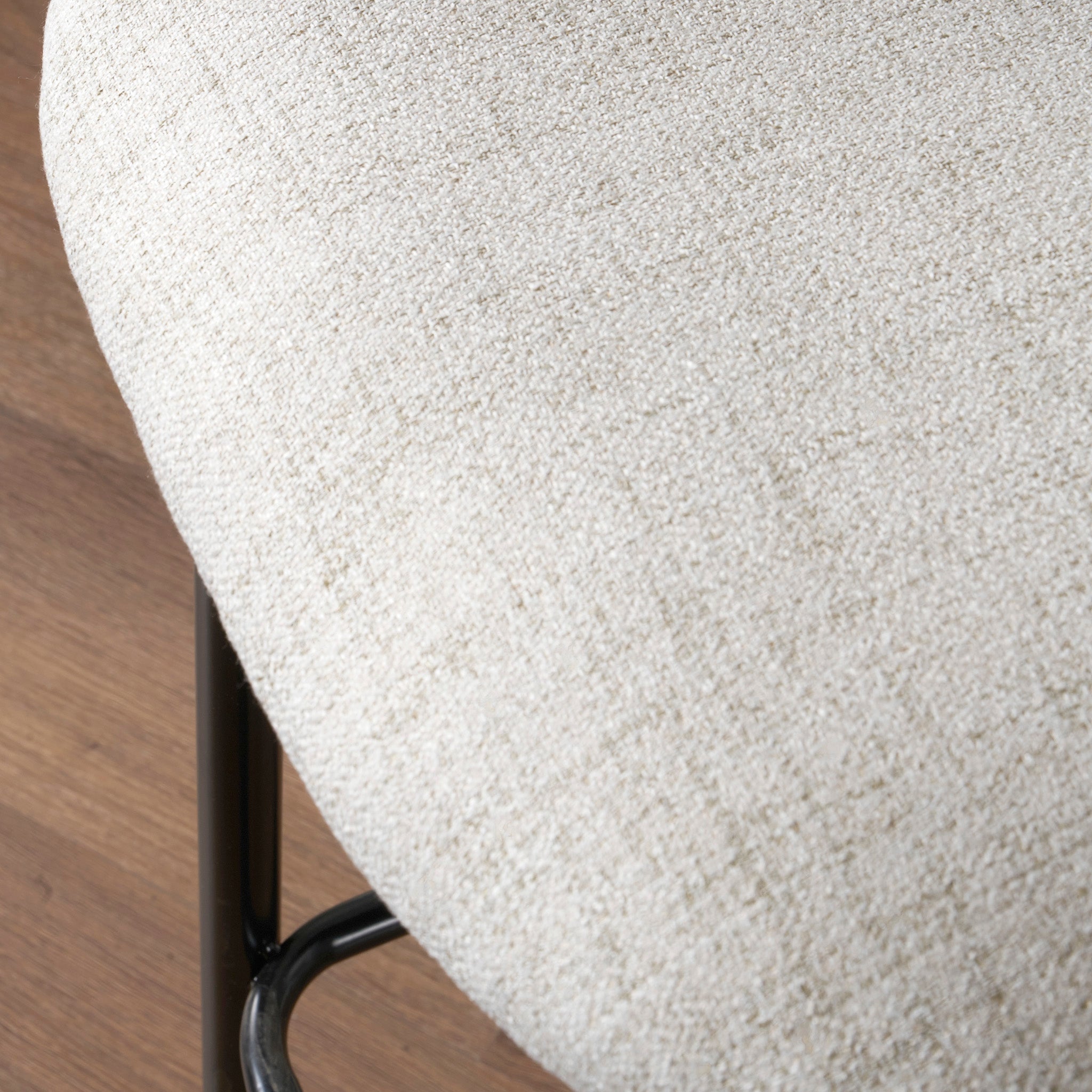 Close-up of the seat of a beige Turi Pebble Linen Mix and Black Metal Bar Stool, placed on a wooden floor, showcasing its modern style.