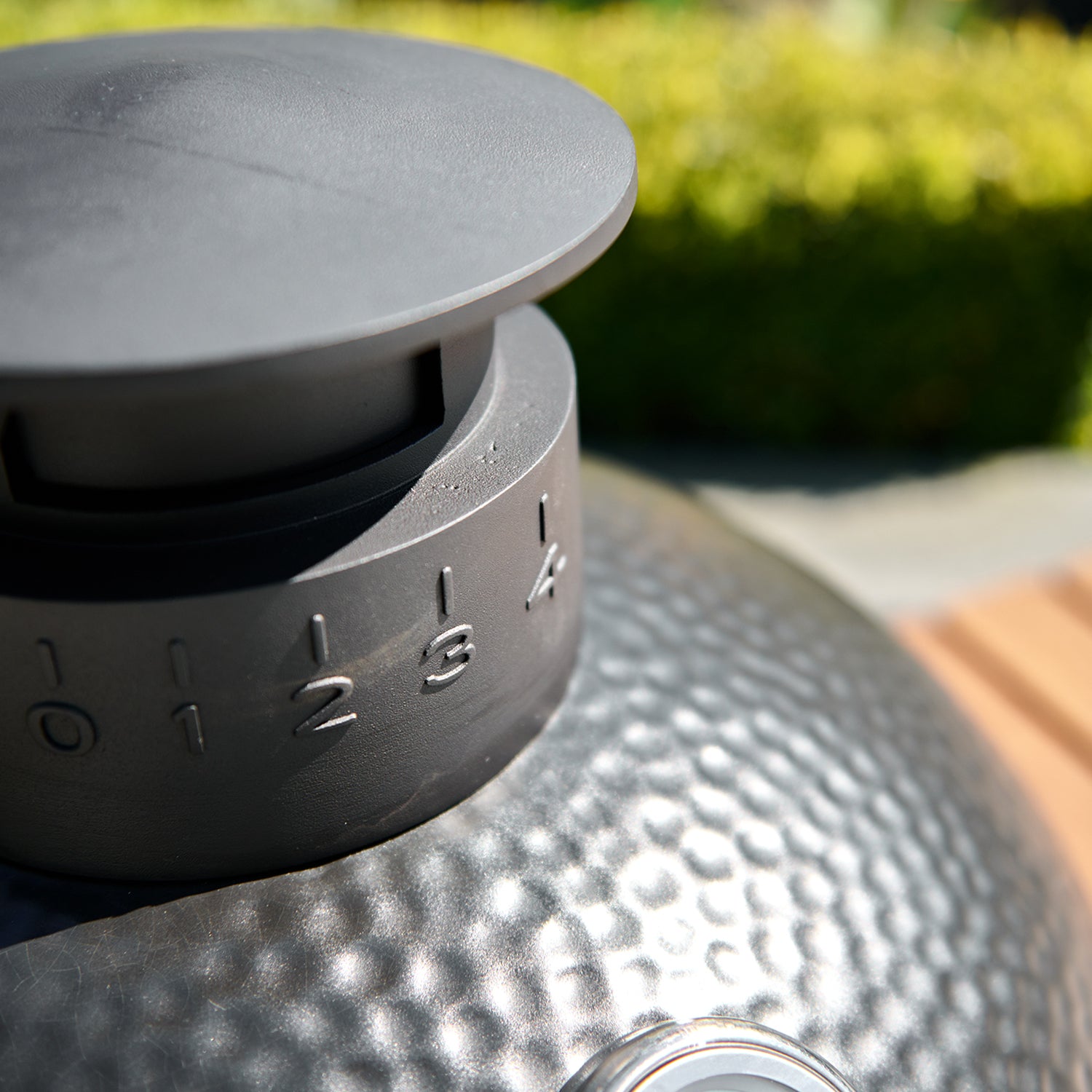 Close-up of a grill vent dial on a Kamado BBQ 22" Ceramic Grill in Black, set to 4 with numbers ranging from 0 to 5, on a textured black surface with a blurred green background.