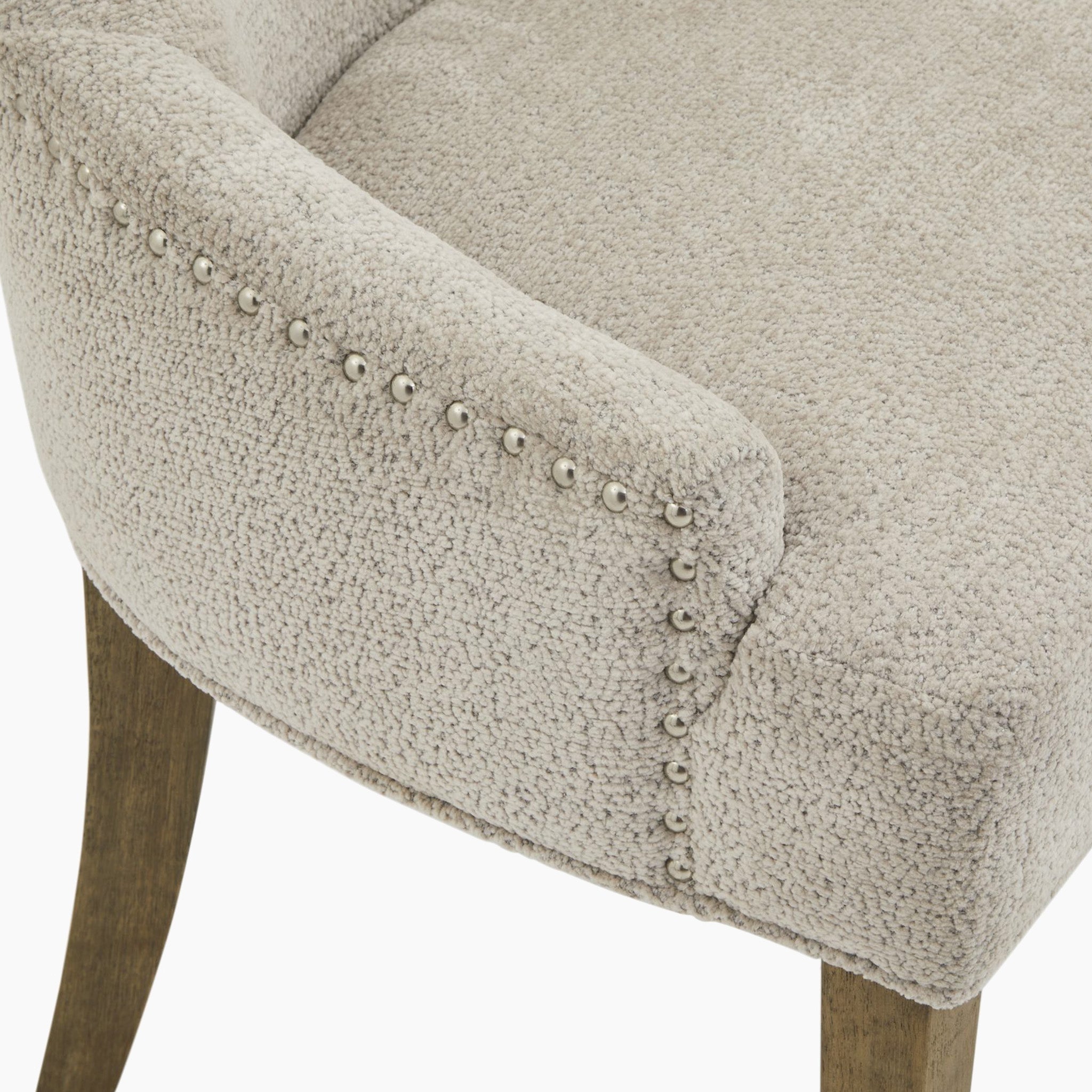 A detailed look at the Brockham Taupe Dining Chair highlights its taupe woven fabric, rubberwood frame, nailhead trim, and wooden legs.