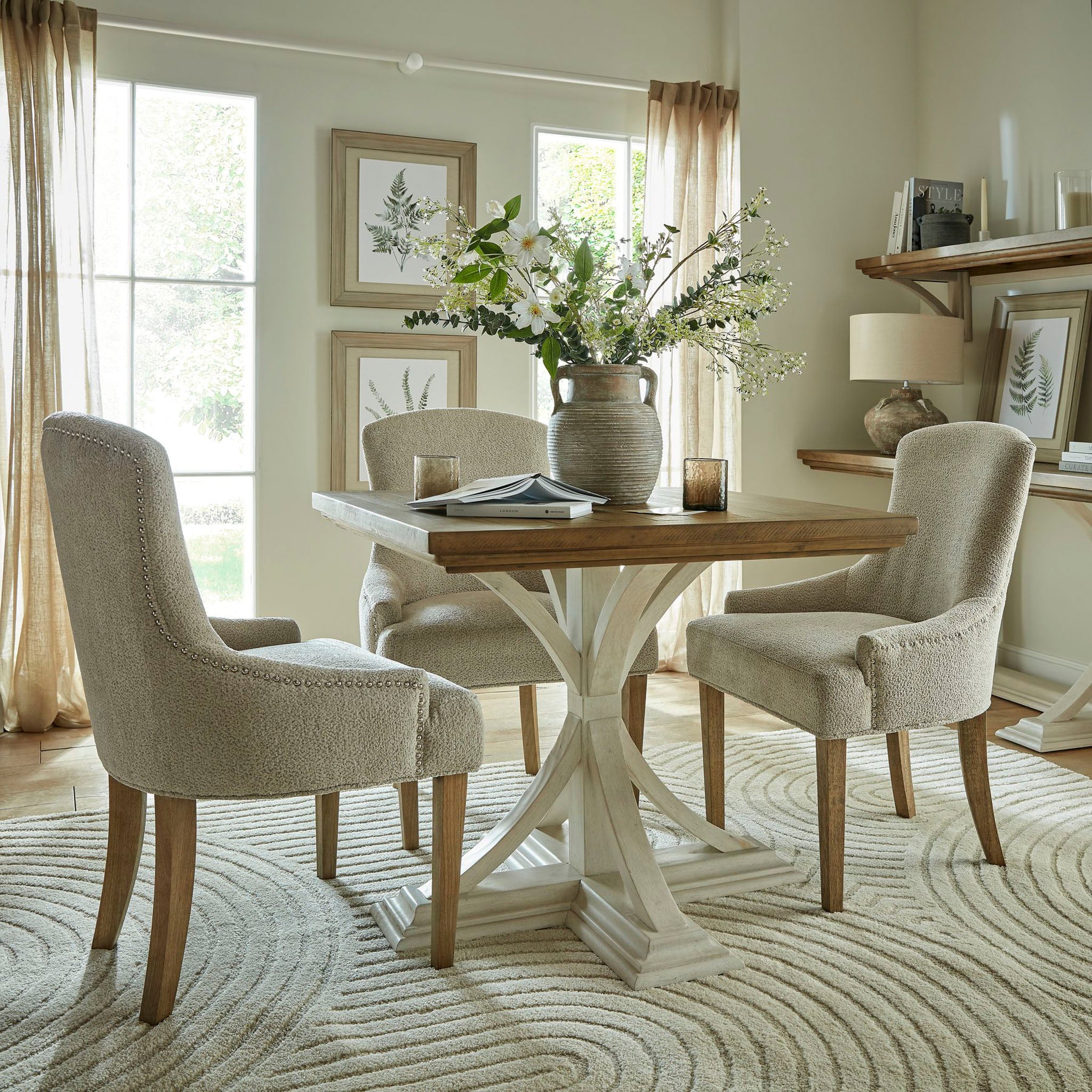 A cozy dining room showcasing a wooden table, four Brockham Taupe Dining Chairs made with taupe woven fabric and robust rubberwood frames, complemented by a vase of flowers, and enveloped in nature-themed decor.