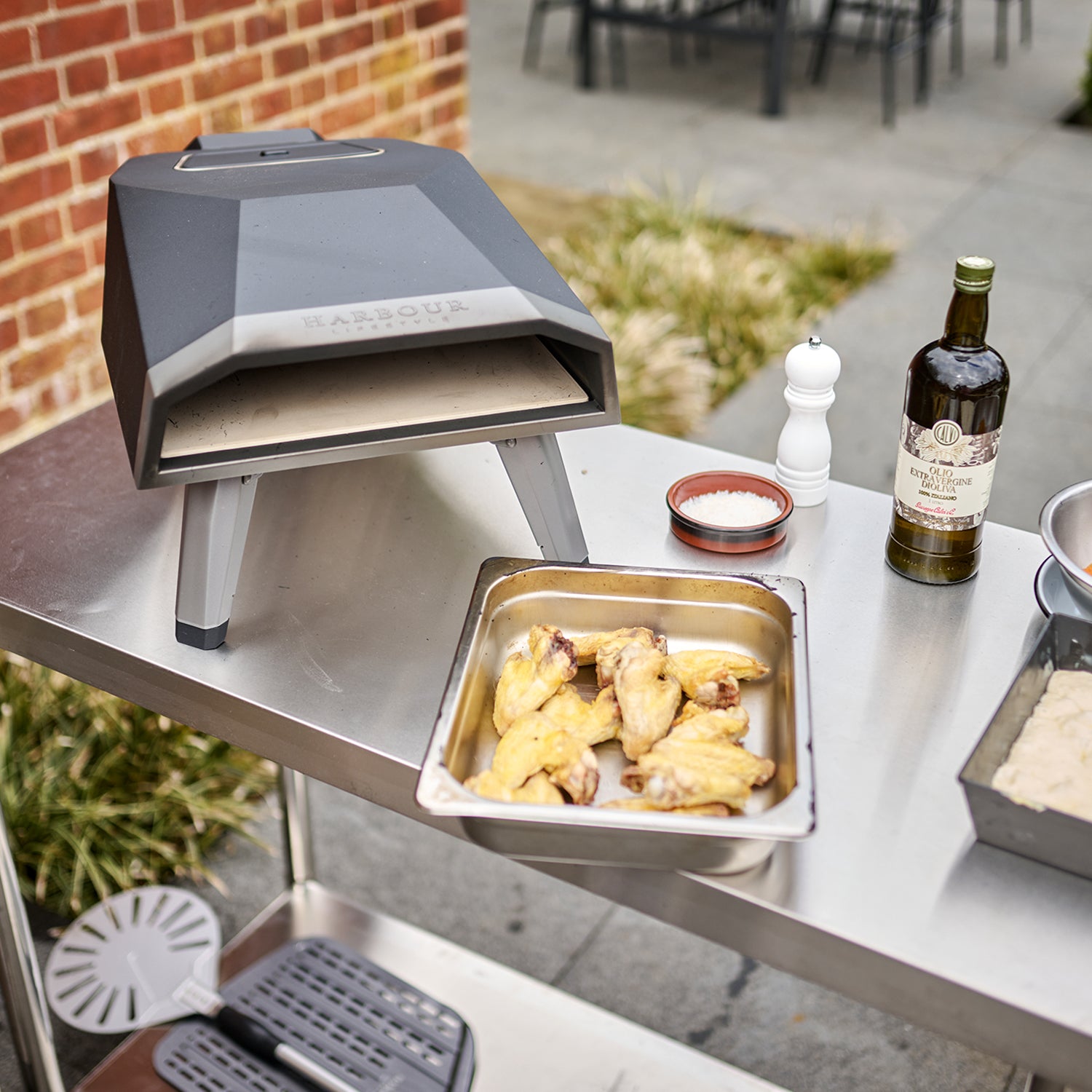 Discover the ultimate stone-baked pizza experience anywhere with the Juno 12" Pizza Oven Bundle with Gas Burner. This portable outdoor pizza oven, set on a robust stainless steel table, comes complete with chicken wings in a tray, a pepper grinder, and a bottle of olive oil. Enjoy deliciously perfect pizzas every time thanks to its durable stainless steel construction.