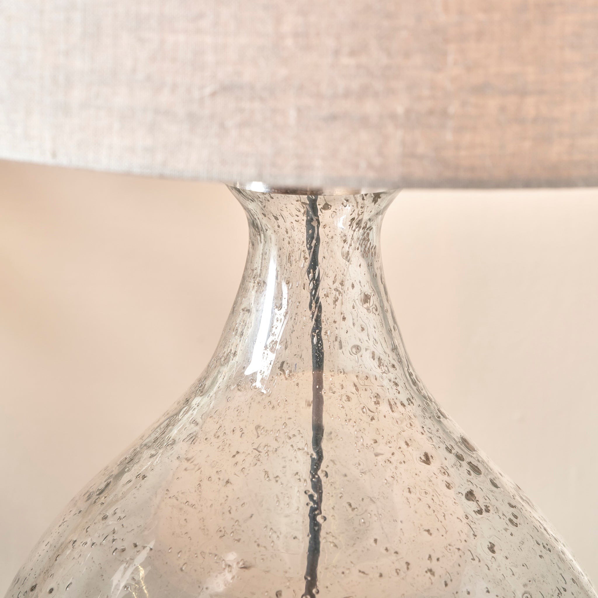 Close-up of the Elysia Bubble Glass and Silver Metal Curved Table Lamp, featuring an organic-shaped clear bubble glass base paired with a textured linen lampshade.