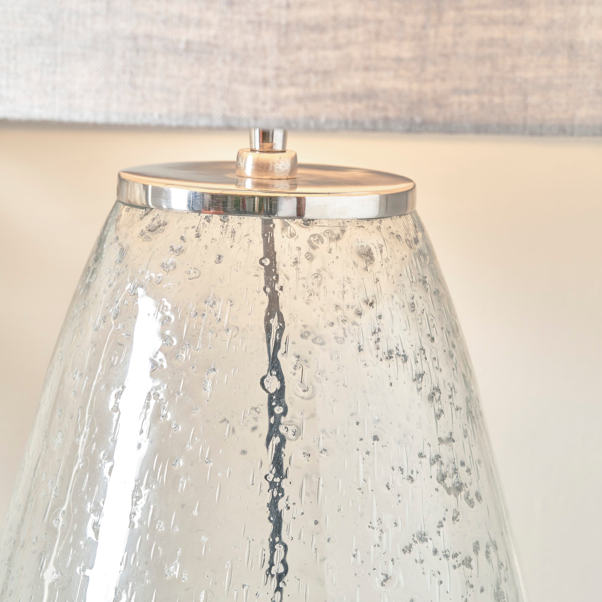 A close-up of the Elysia Bubble Glass and Silver Metal Table Lamp, featuring a textured surface and silver metal trim, set against a light gray backdrop.