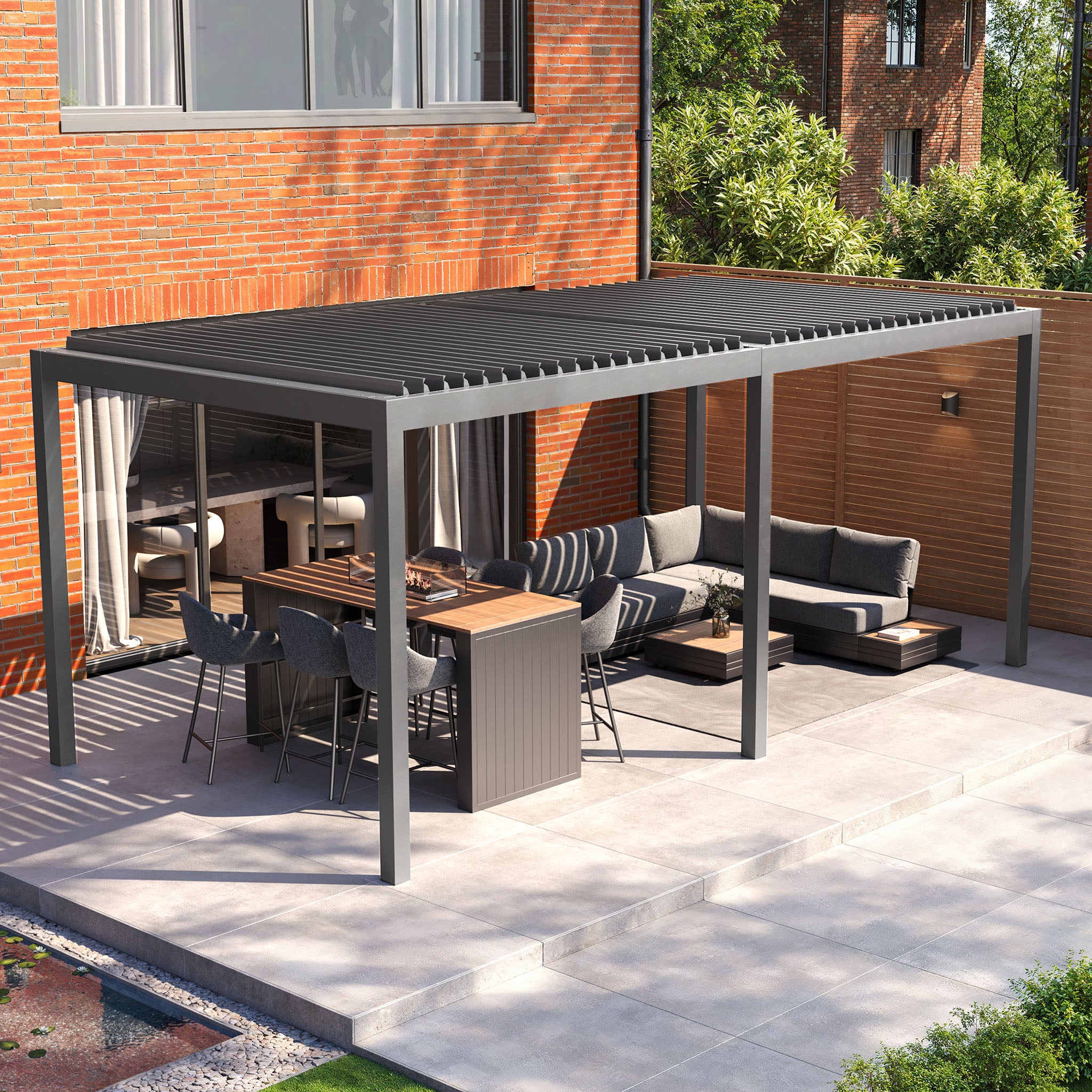 A modern patio with a 3m x 6m PergoSTET Deluxe pergola in grey, complete with motorized LED louvres, stylish outdoor furniture, and a dining table set against a charming brick wall and lush greenery.