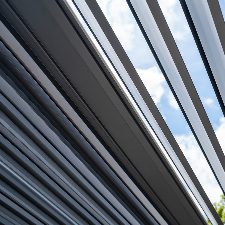 Close-up of a PergoSTET Deluxe Frame Only 3m x 3m Square Pergola Extension with Motorised LED Louvres in Grey against a blue sky with clouds.