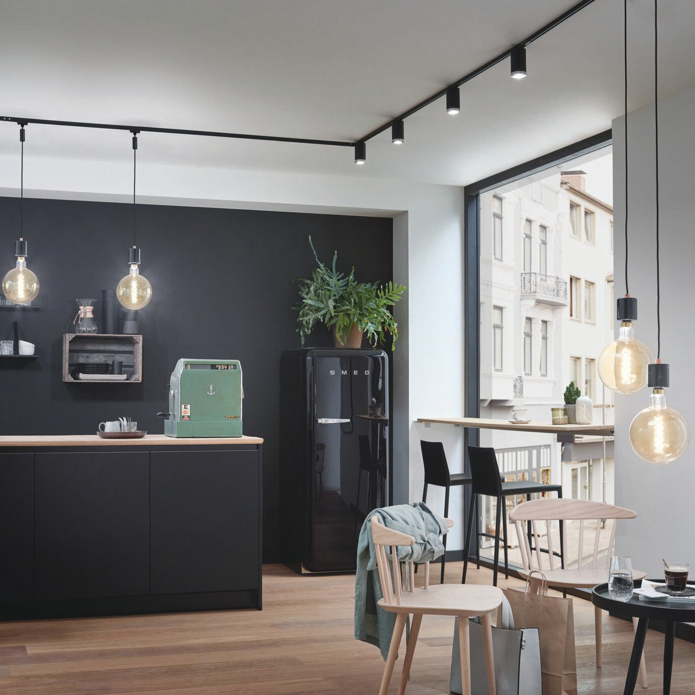 Modern kitchen featuring hanging lights with a Paulmann Standard Reflector Bulb 7W GU10 Warm White, black cabinets, a green mixer, bar stools by the window, and wooden chairs.