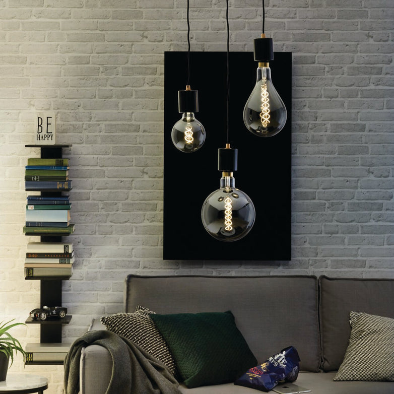 Create a cozy living room ambiance that blends modern style with vintage charm, showcasing hanging Edison bulbs alongside the Paulmann Filament LED Globe Bulb 4W E27 in Gold Glass for a warm, inviting glow. A stack of books is artfully arranged next to a "Be Happy" sign, while resting above an inviting gray sofa adorned with plush cushions.