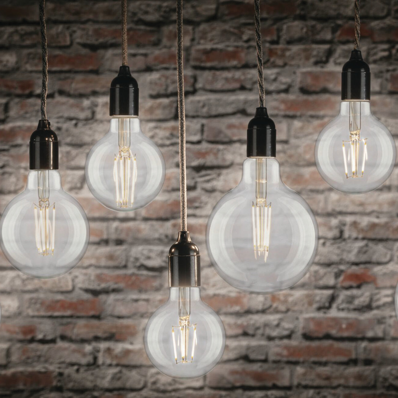 Five Paulmann Filament LED Globe Bulbs, each with a 7.5W E27 base, hang gracefully against a textured brick wall, showcasing their vintage-style design in neutral white.