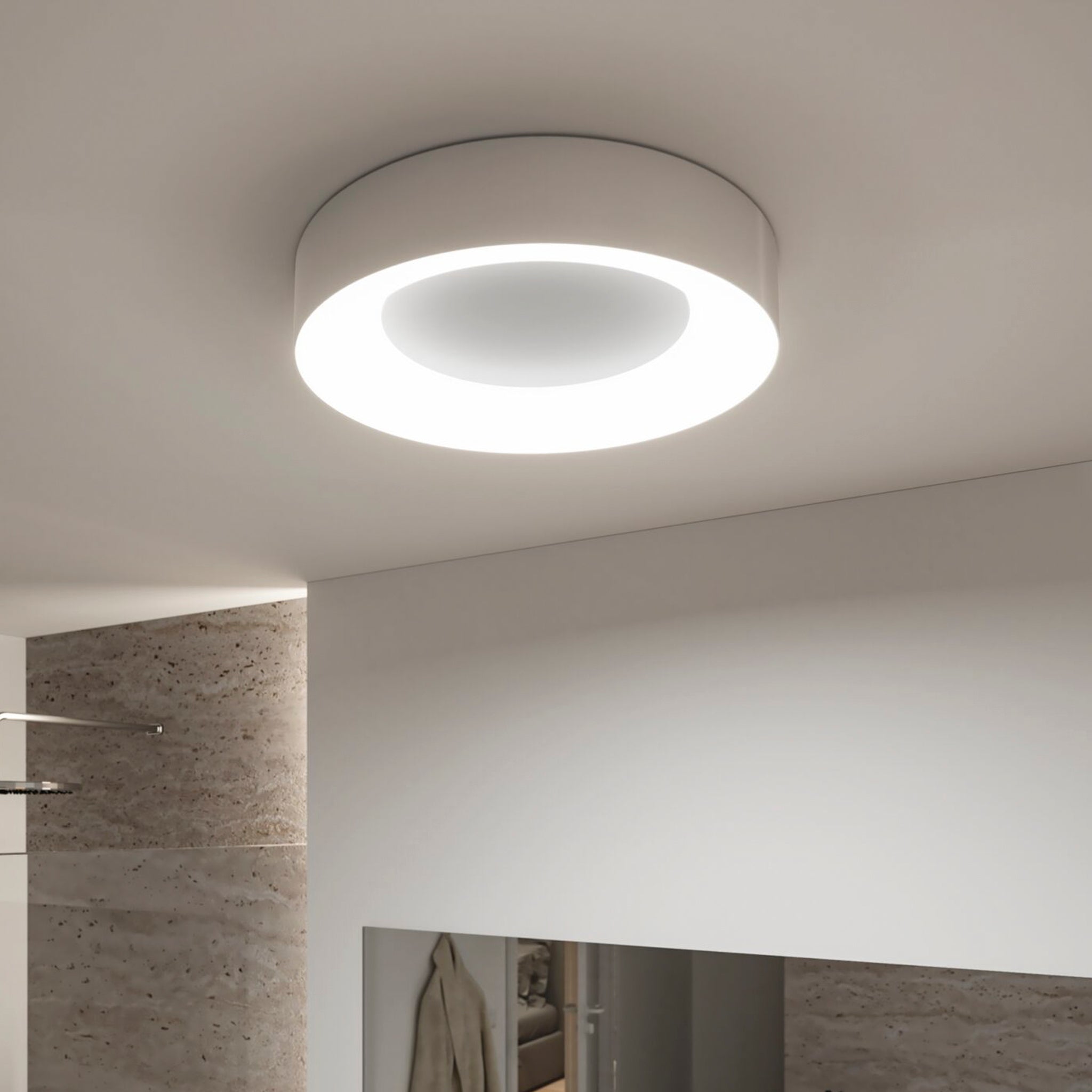 A modern Casca 25W LED Switch 2100lm Ceiling Light in Matt Aluminium, with its bright ring of illumination, installed in a room with beige walls, creates a special lighting effect.