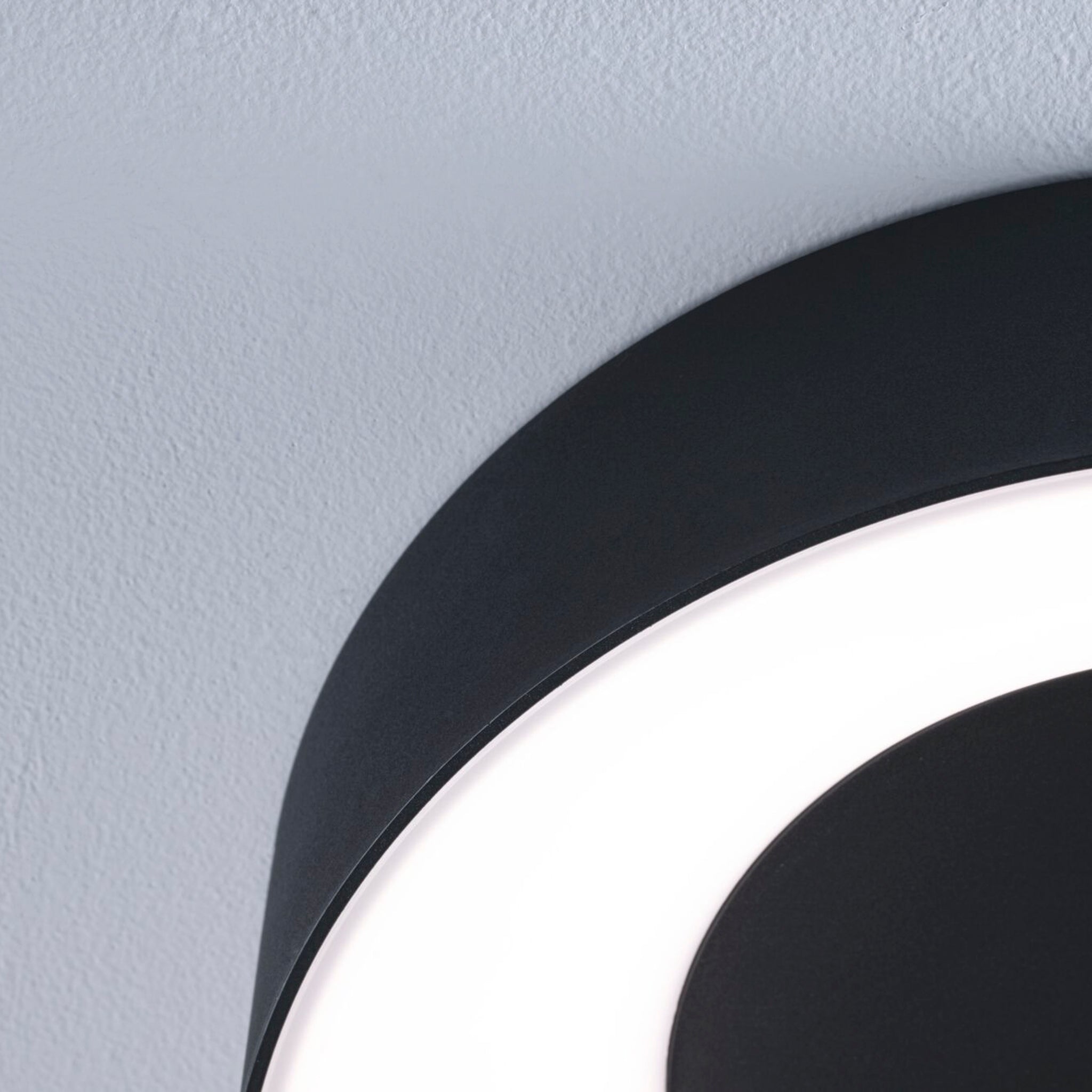 Close-up of a modern Casca 18W LED Switch 1500lm Ceiling Light in Black Matt mounted on a light grey textured ceiling, casting a special lighting effect.