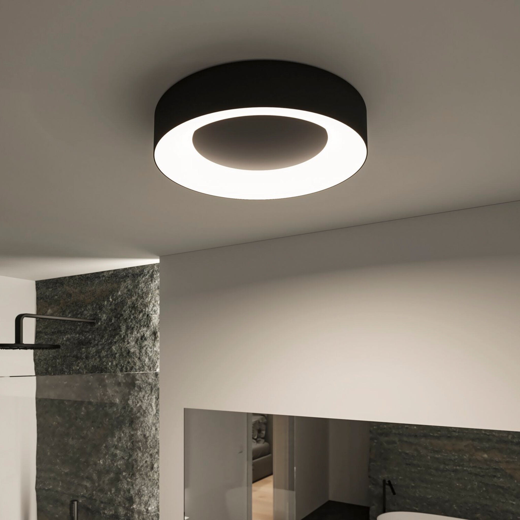 The Casca 25W LED Switch 2100lm Ceiling Light in Black Matt illuminates a minimalist room with stone-textured walls and sleek decor, offering an adjustable light colour to enhance the lighting effect.