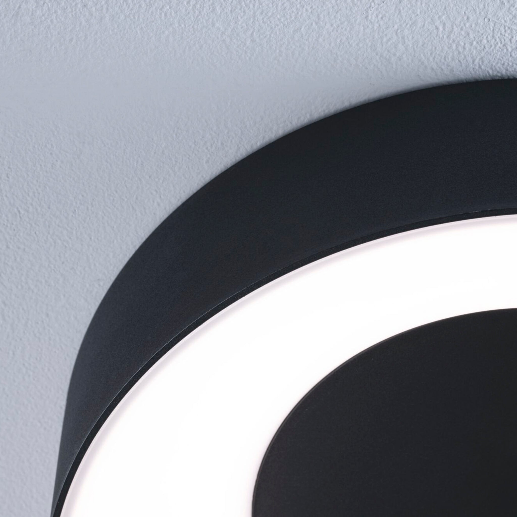 Close-up of a modern Casca 25W LED Switch 2100lm Ceiling Light in Black Matt with a curved design against a light-colored ceiling, offering an adjustable light color for enhanced lighting effect.