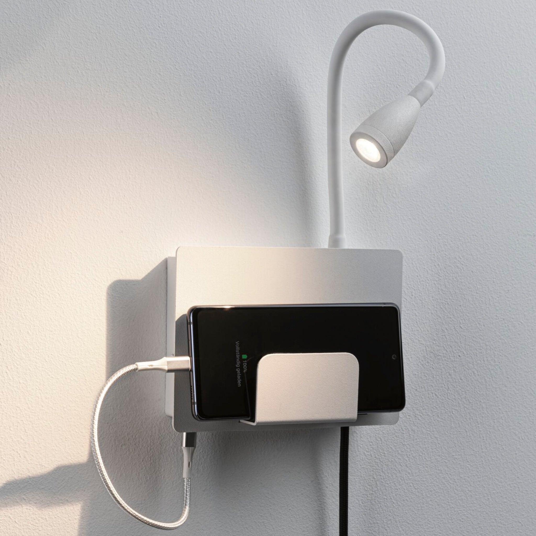 The Halina 3.5W LED Wall Light with USB Charging Port in White Matt is a wall-mounted phone holder featuring an attached flexible luminaire arm and a USB Type-C socket, perfect for reading.