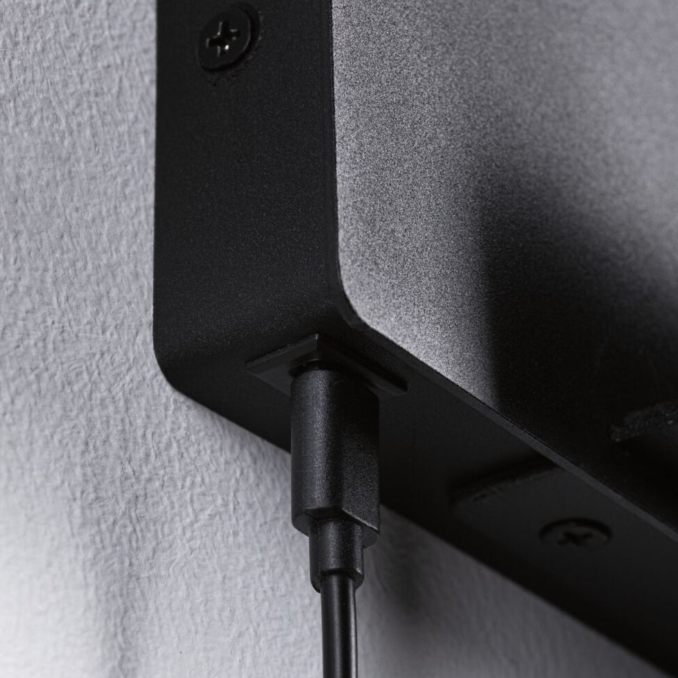 Close-up of a black power cable plugged into a Halina 3.5W LED Wall Light with USB Charging Port in Black Matt, mounted on a textured white wall.