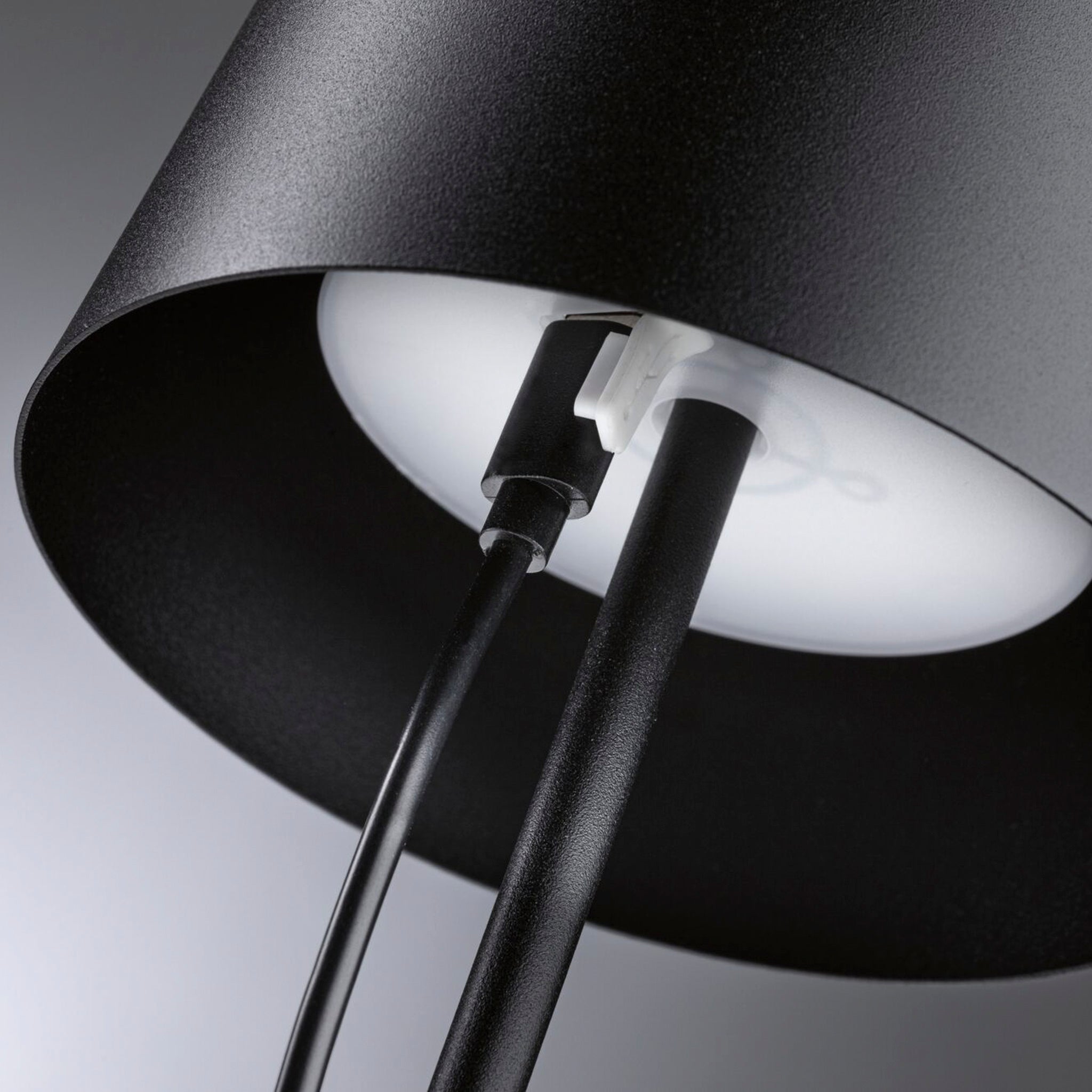 Close-up of the Gilo 2.8W LED Mobile Dimmable Floor Lamp in Black Matt, featuring a black lampshade with a white interior. The portable battery-powered lamp's power cord is connected to the bulb socket, offering continuous touch dimming function for an ideal warm white lighting mood.