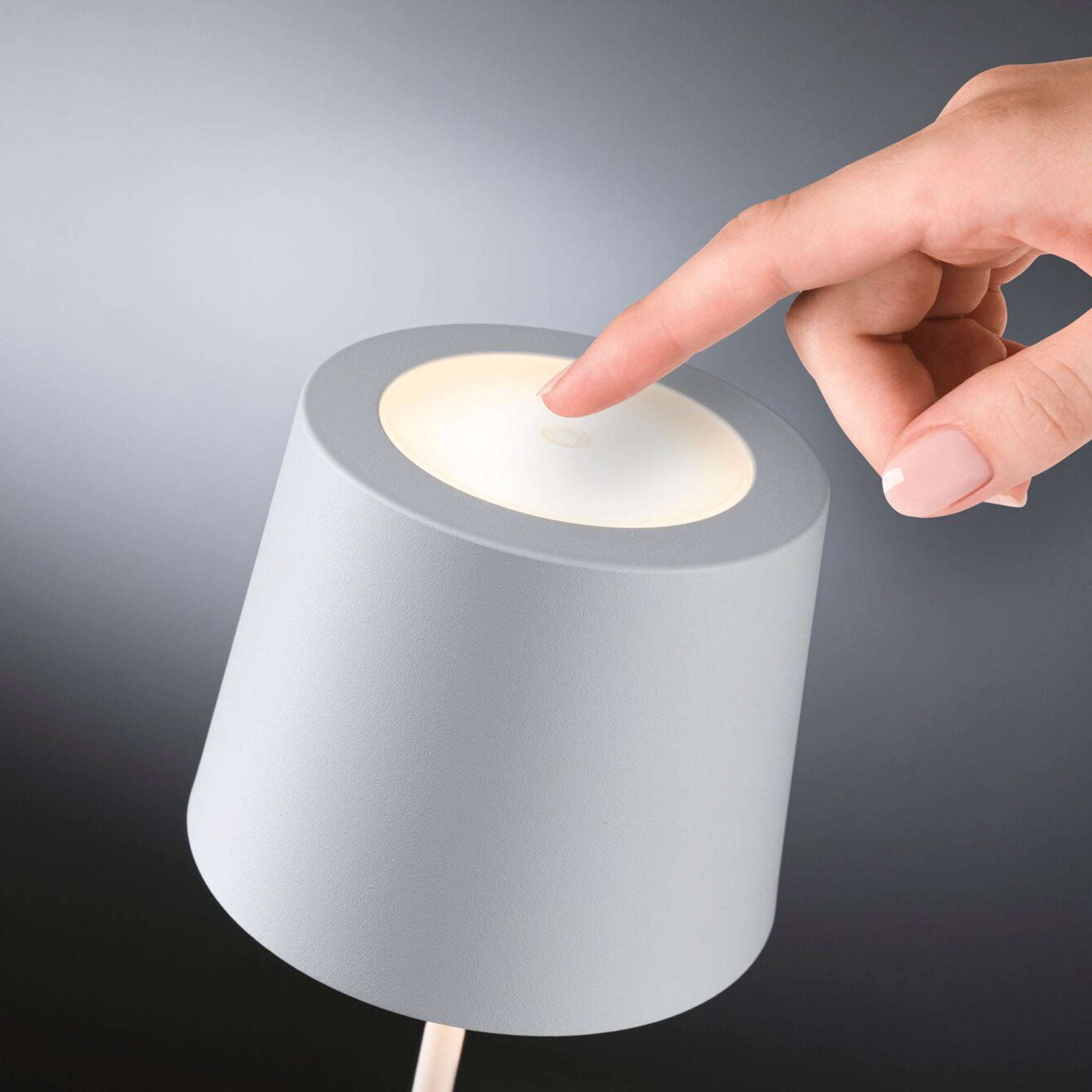 A hand touching the top of a white, cylindrical Gilo 2.8W LED Mobile Dimmable Floor Lamp with a soft light.