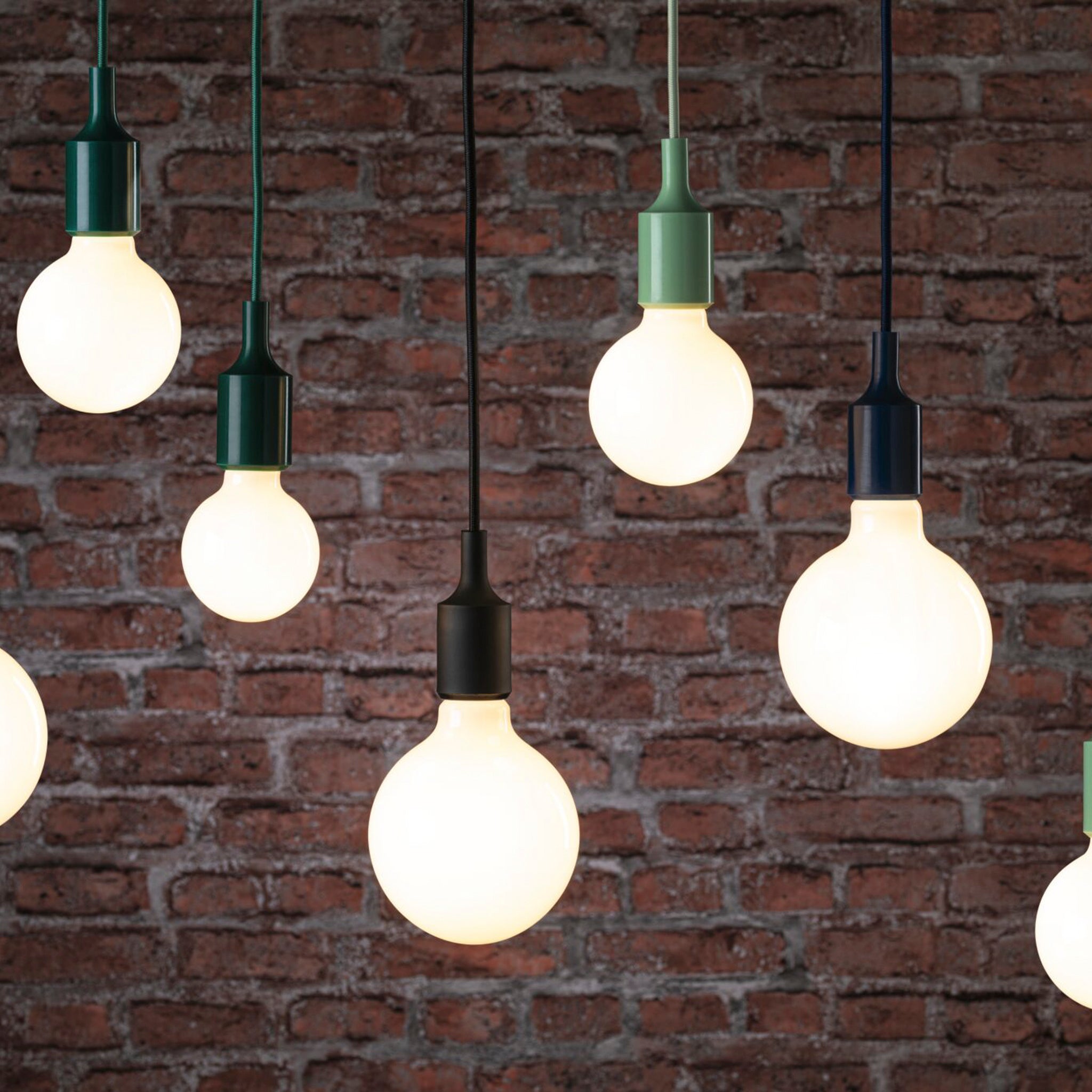 The Neordic Ketil 60W Dimmable Pendant Light from Paulmann, featuring light green fixtures, casts a warm glow against the backdrop of a red brick wall.