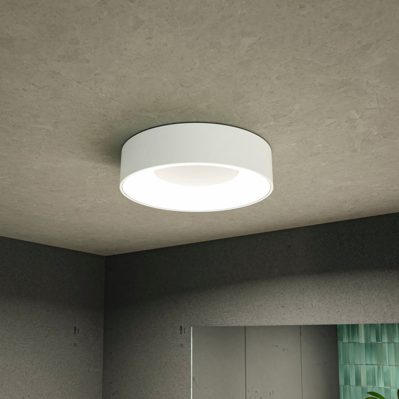 The Casca 18W LED Switch 1500lm Ceiling Light in White is installed on a plain ceiling in a contemporary room, offering an adjustable light color to create a special lighting effect.