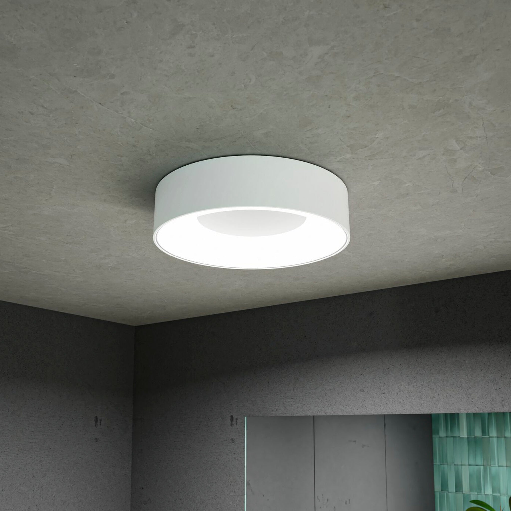 The Casca 18W LED Switch 1500lm Ceiling Light in White is illuminated, casting a special lighting effect against a textured gray ceiling.