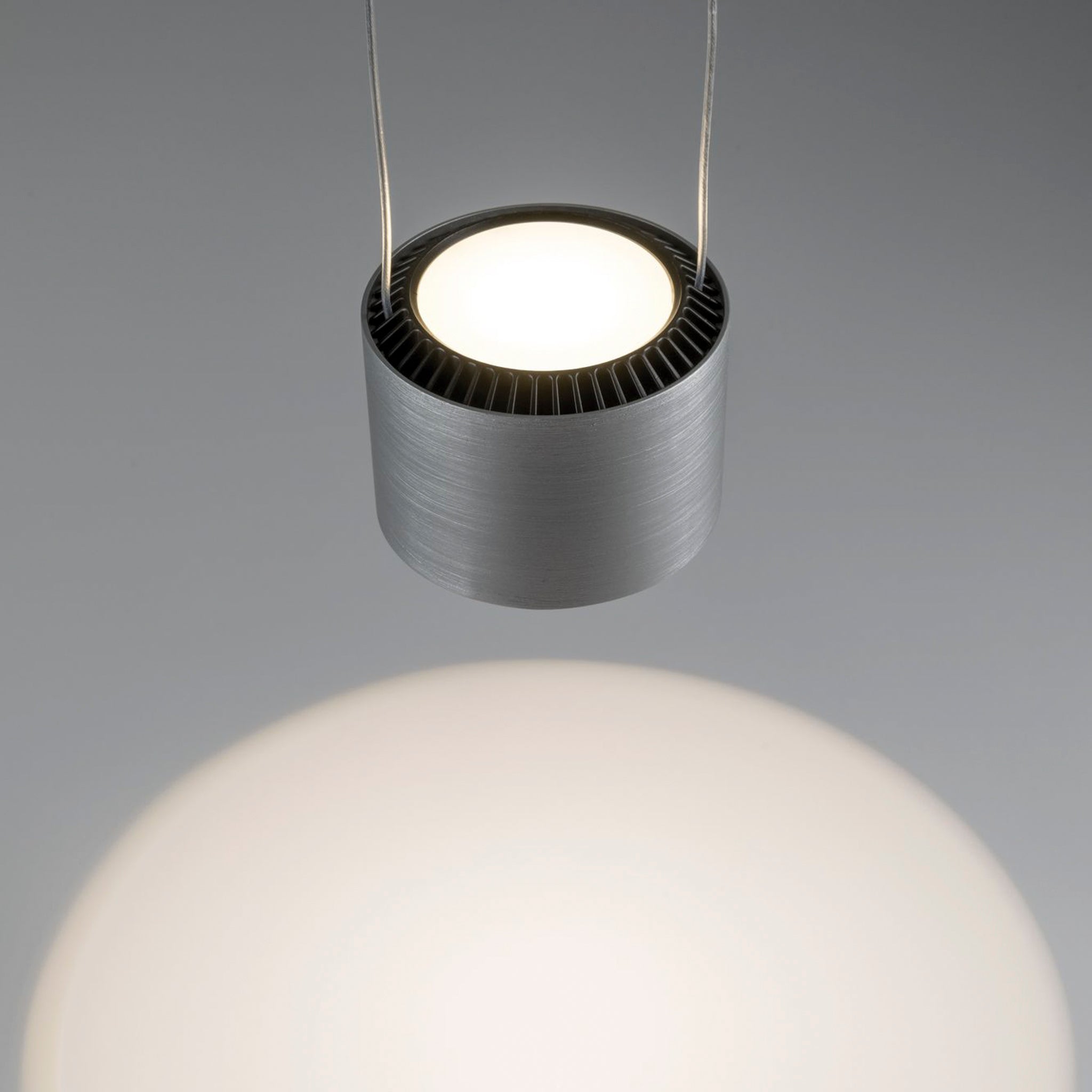 Close-up of the Aldan 28W LED Dimmable 3 Lamp Pendant Light in Brushed Aluminium, featuring adjustable pendant lengths and cylindrical shades, emitting a bright, focused beam over a softly lit area below.