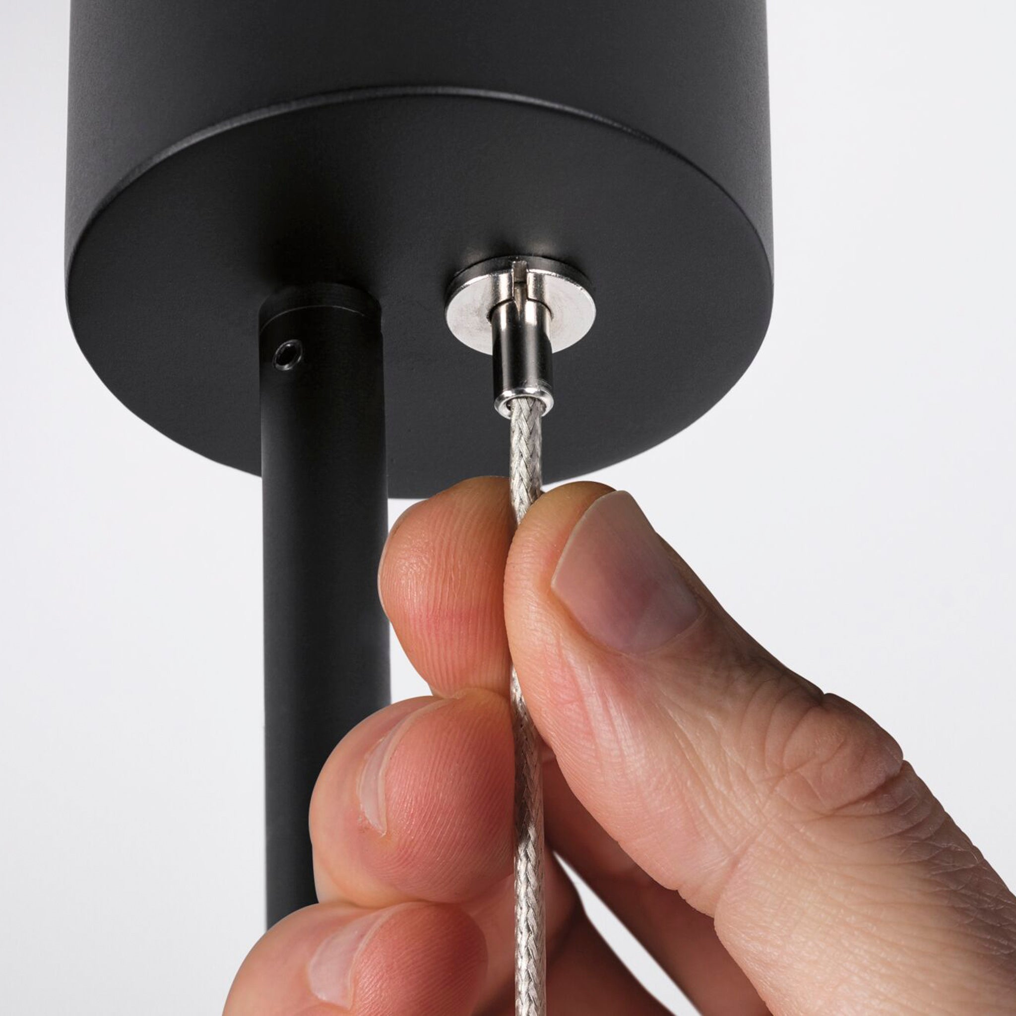 Close-up of a hand adjusting a cable connected to the Paulmann - Puric Pane 6W LED Dimmable Smart Home Zigbee 3.0 Pendant Light in Black, part of a smart luminaire system.