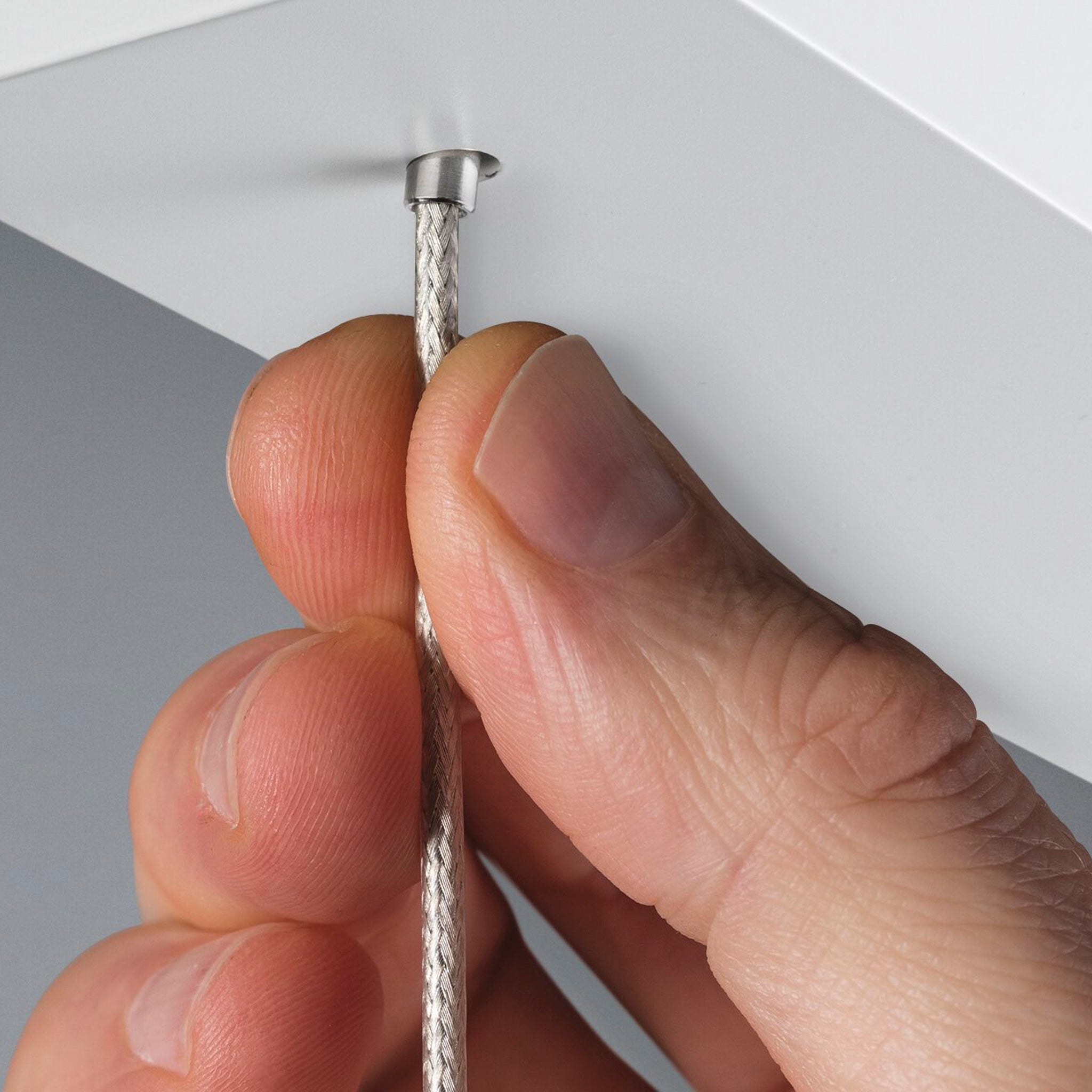 Close-up of a hand adjusting a braided wire secured by a small metal hook on the height-adjustable Paulmann Lento 37W LED Dimmable Pendant Light in White.