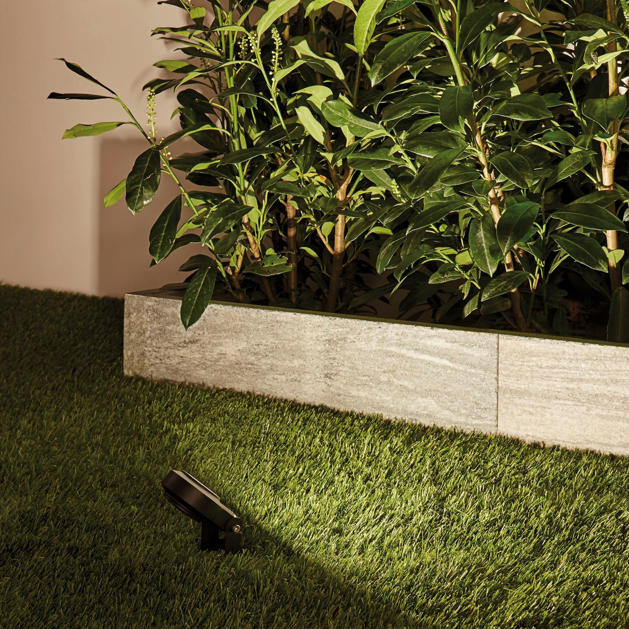 Paulmann's Plug & Shine Outdoor Sting 18W LED Warm White Expansion Set in Anthracite illuminates green plants and manicured grass beside a weather-resistant concrete border at night.