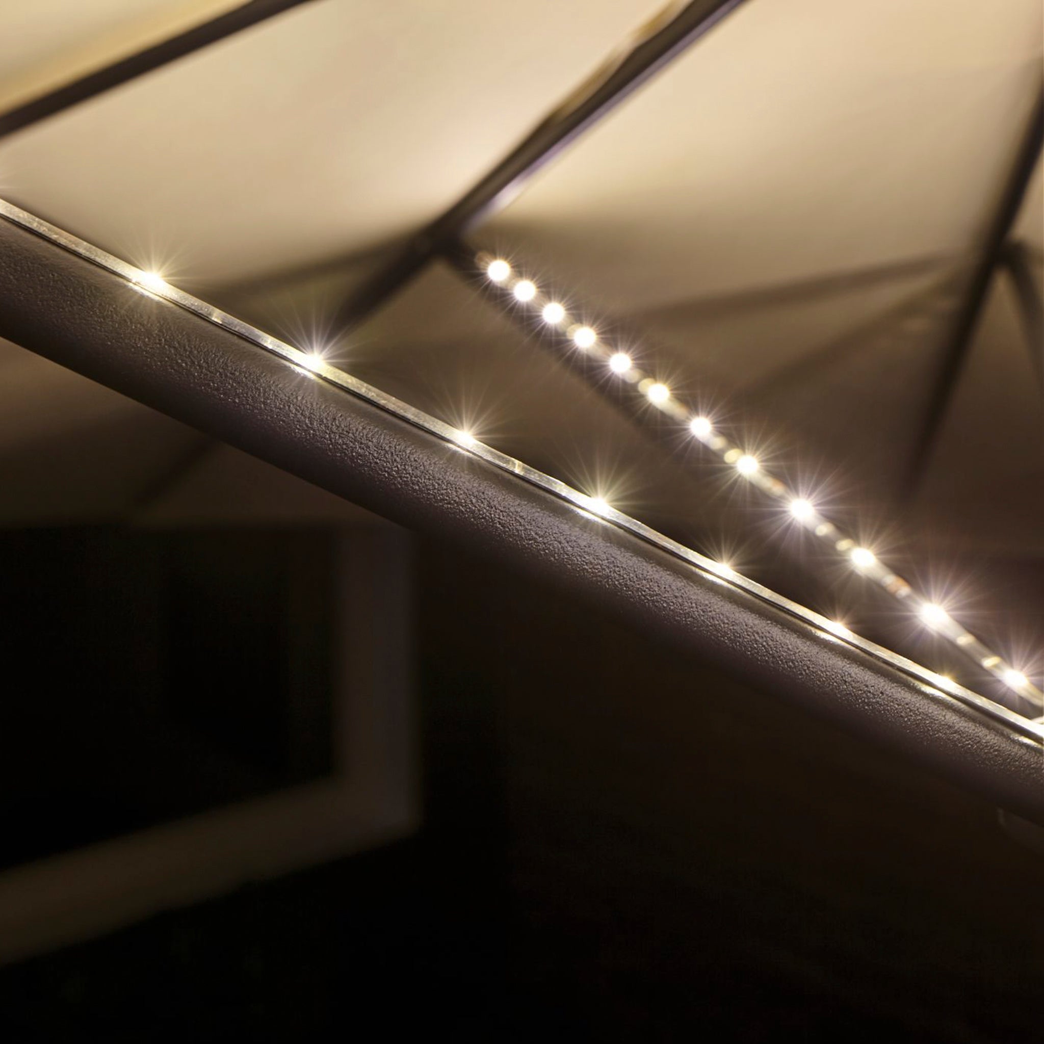 A close-up of the Paulmann Outdoor LED 4x40cm Parasol Strips in Black glowing beneath a tent canopy at night, creating the perfect ambience for a cosy outdoor gathering. The flexible self-adhesive design ensures easy setup and enhances the inviting atmosphere.