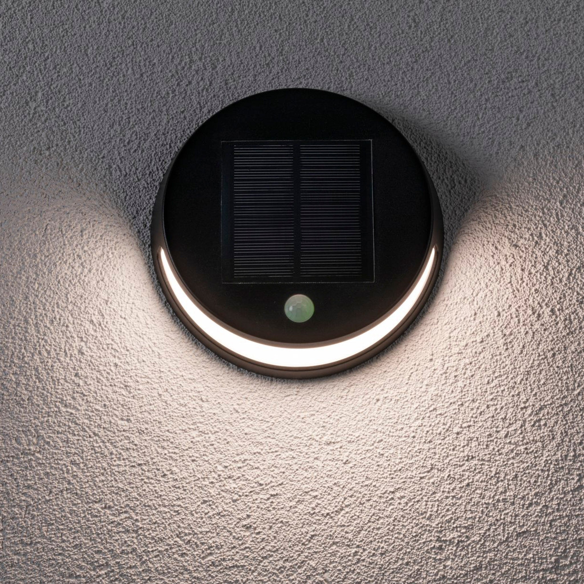 The Paulmann Outdoor Helena 3W LED Solar Wall Light with Motion Detection in black elegantly illuminates a textured gray exterior wall.