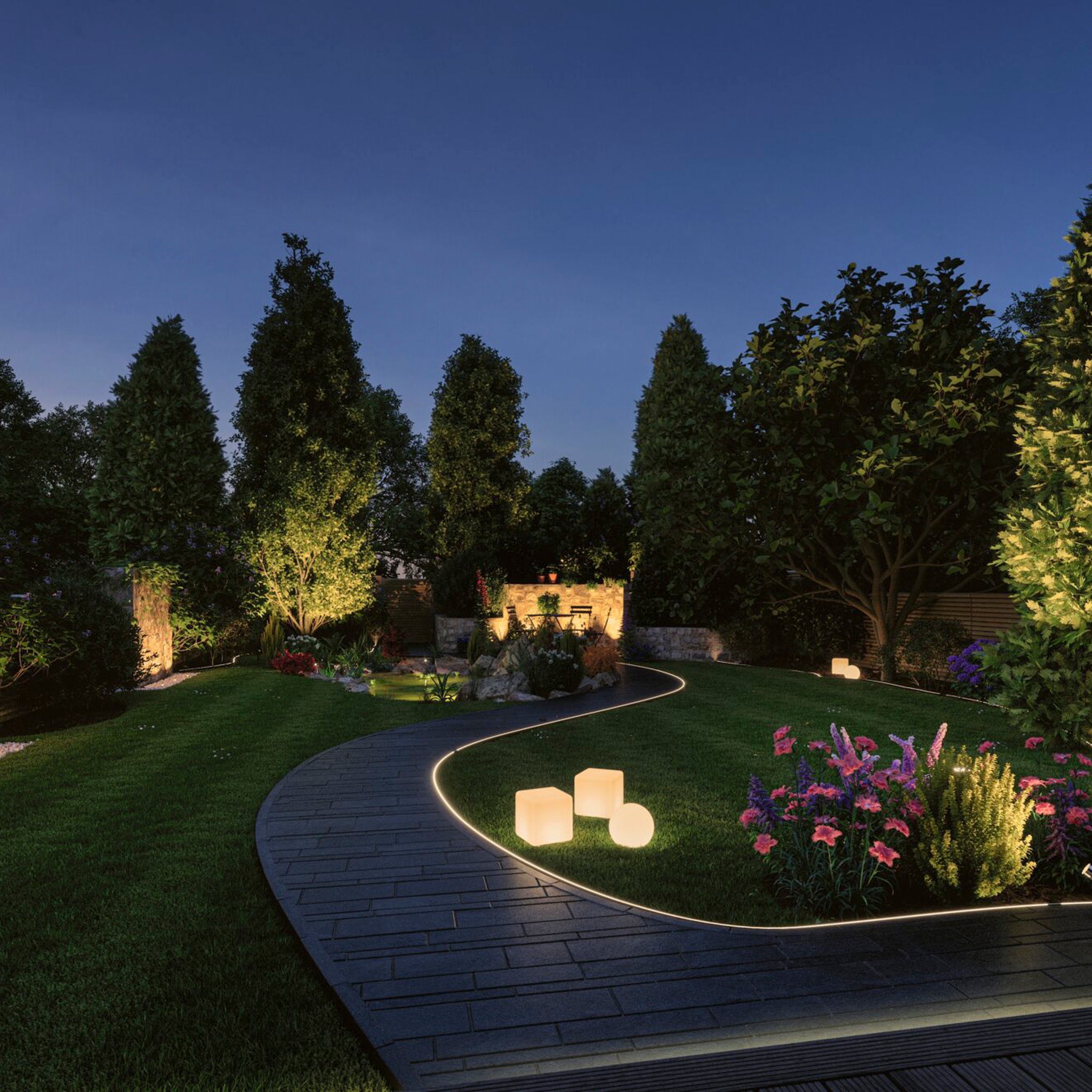 A beautifully lit garden at night, enhanced by LED Garden Spotlights along a curved path, features glowing orbs and colorful flowers surrounded by tall trees, all powered seamlessly with the Paulmann - Plug & Shine Outdoor 30VA Power Supply Transformer in White.