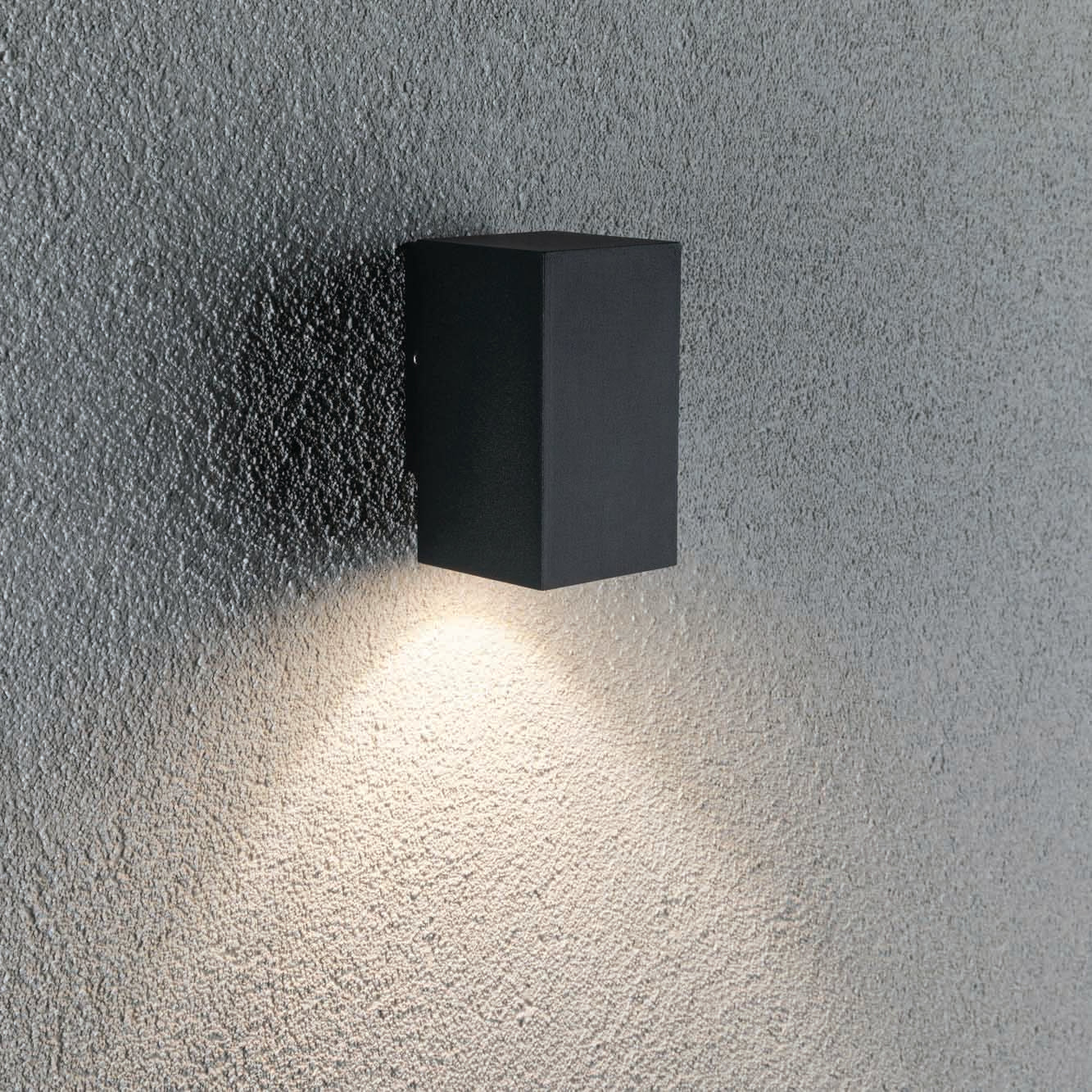 The Outdoor Flame 5.2W LED Single Output Wall Light in Anthracite casts light downwards onto a textured gray wall, creating a modern and elegant effect.