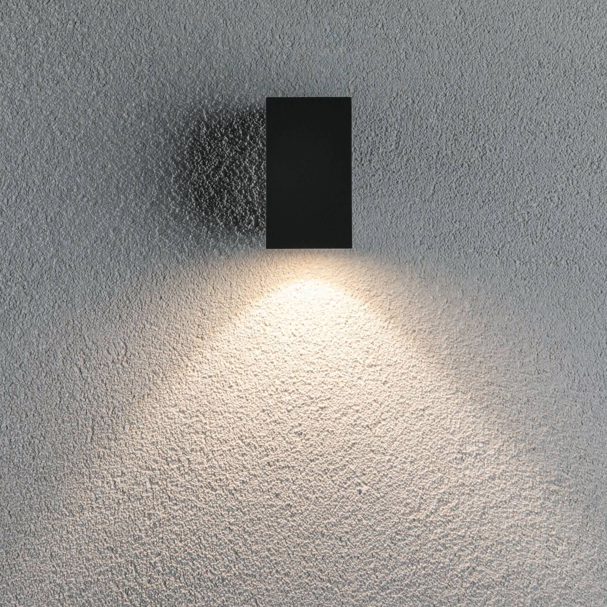 An Outdoor Flame 5.2W LED Single Output Wall Light in Anthracite, surface-mounted, casts a soft, triangular light pattern on a gray textured wall.