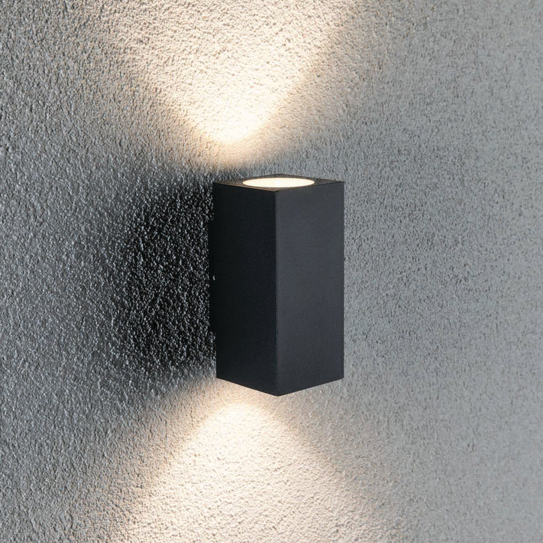 The Outdoor Flame 6.6W LED Dual Output Wall Light in Anthracite casts light both upward and downward against a textured gray wall, creating attractive lighting effects.