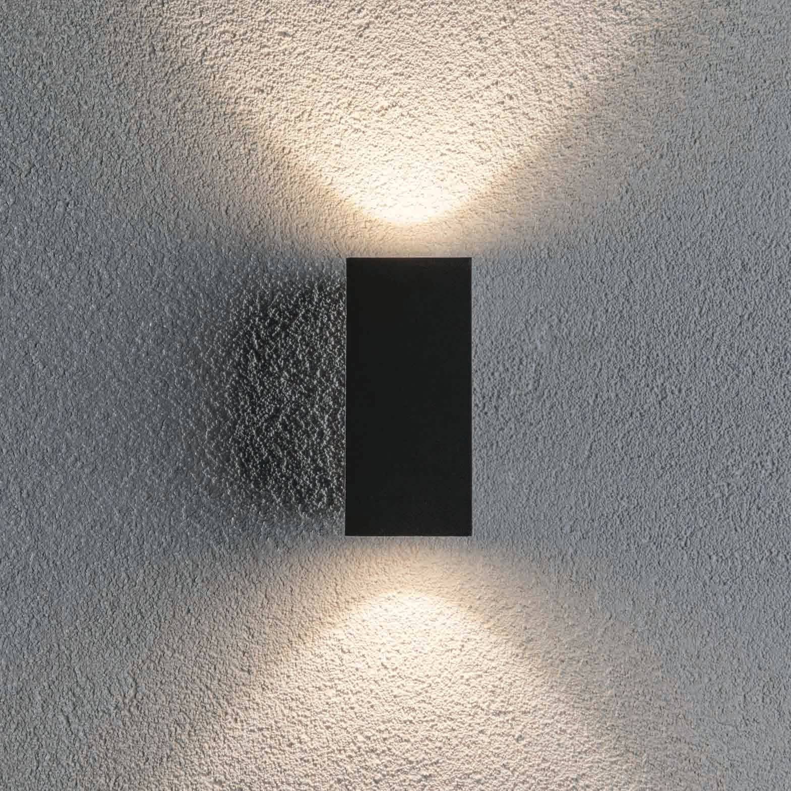 The Outdoor Flame 6.6W LED Dual Output Wall Light in Anthracite casts light both upwards and downwards on a textured wall, creating attractive lighting effects with advanced LED technology.