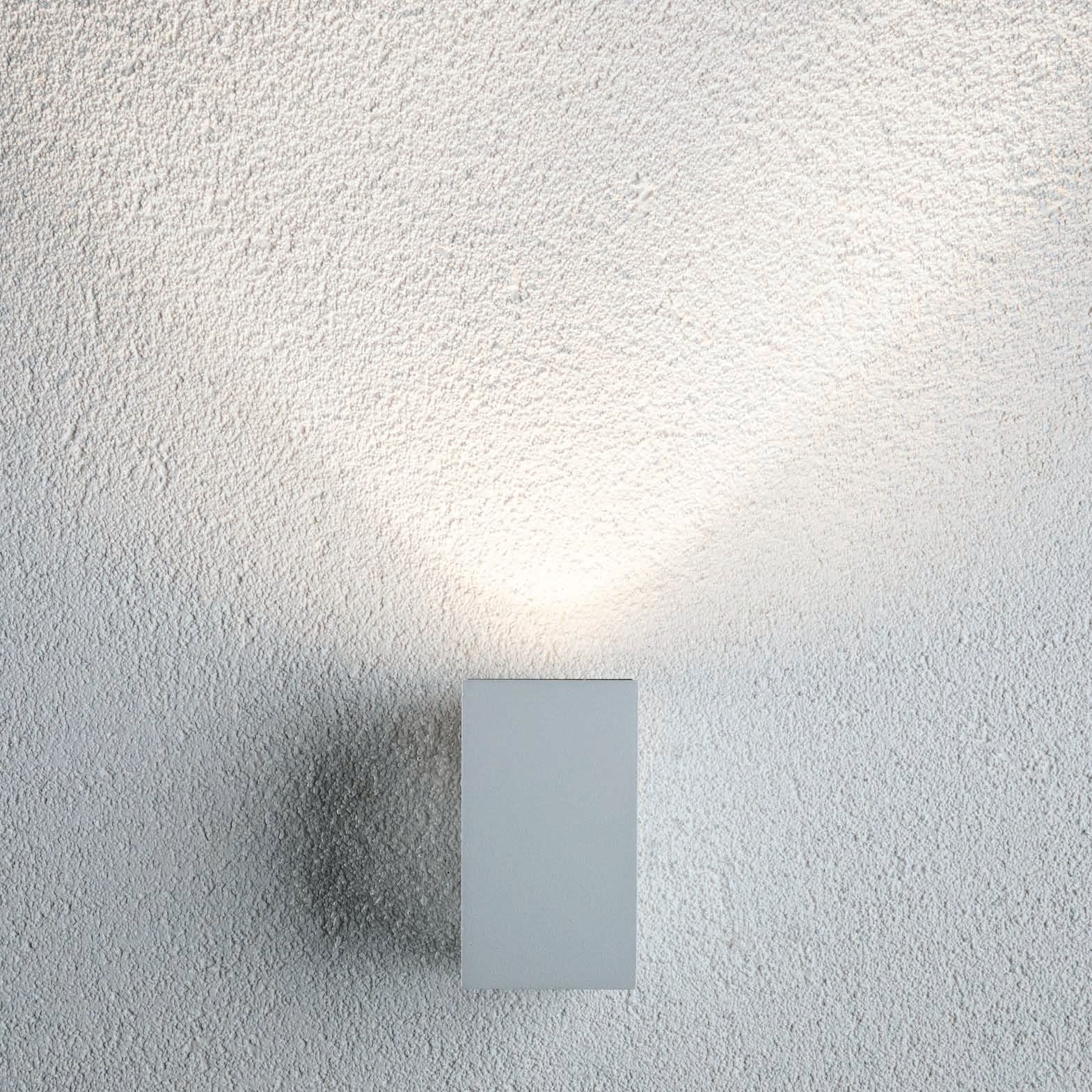 The Paulmann - Outdoor Flame 5.2W LED Single Output Wall Light in White casts a soft glow on the textured white wall, enhanced by modern LED technology.