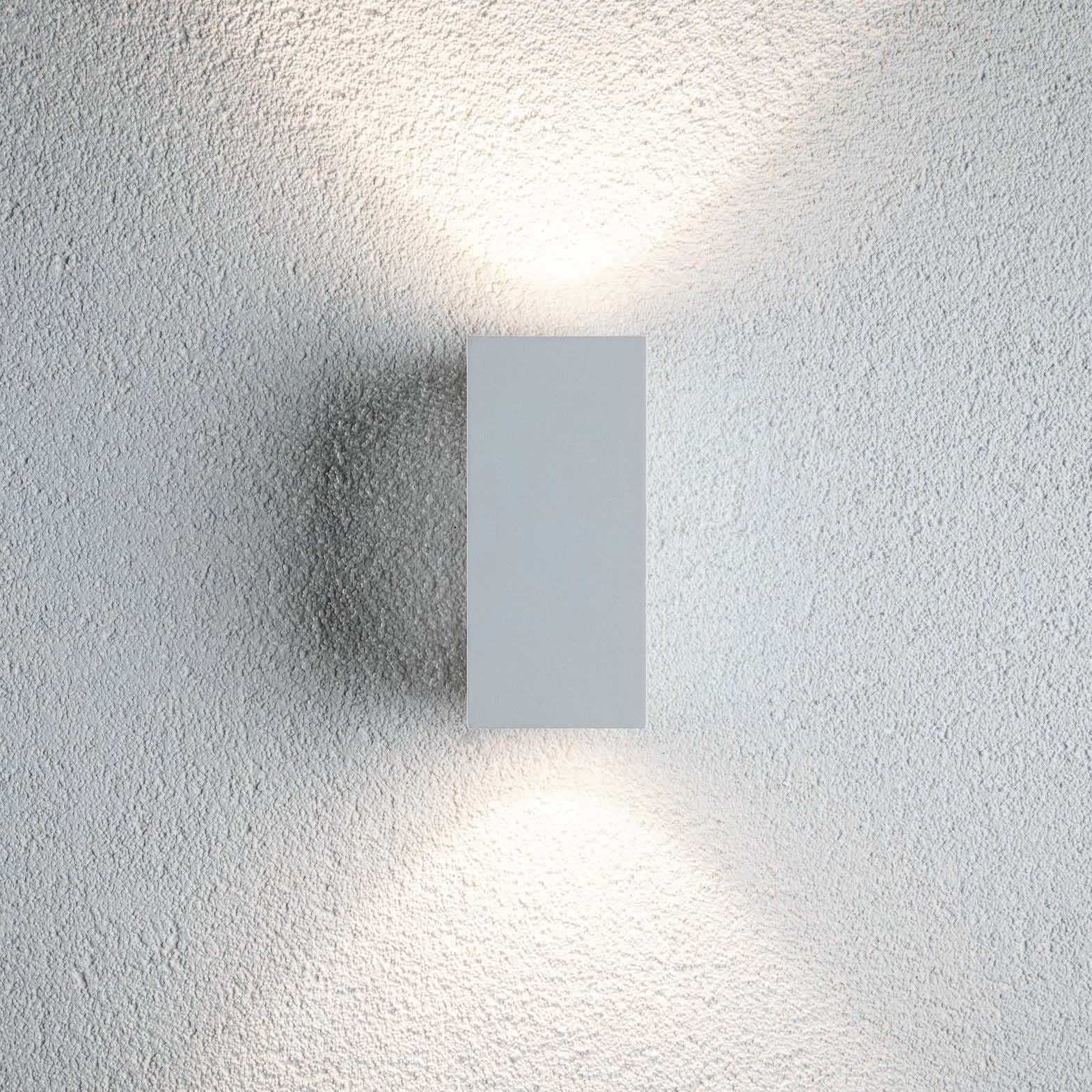 The Outdoor Flame 6.6W LED Dual Output Wall Light in White illuminates a textured surface with attractive lighting effects, projecting light both upwards and downwards.