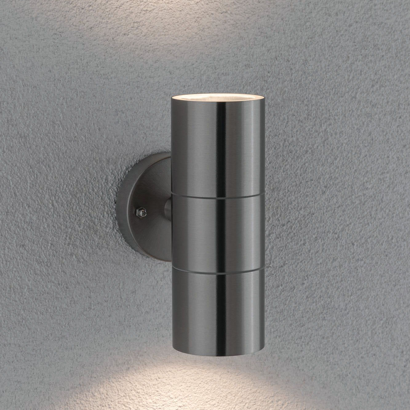 The Paulmann Outdoor Flame 10W LED Dual Output Wall Light in Stainless Steel adorns a textured gray wall, casting captivating lighting effects both above and below.