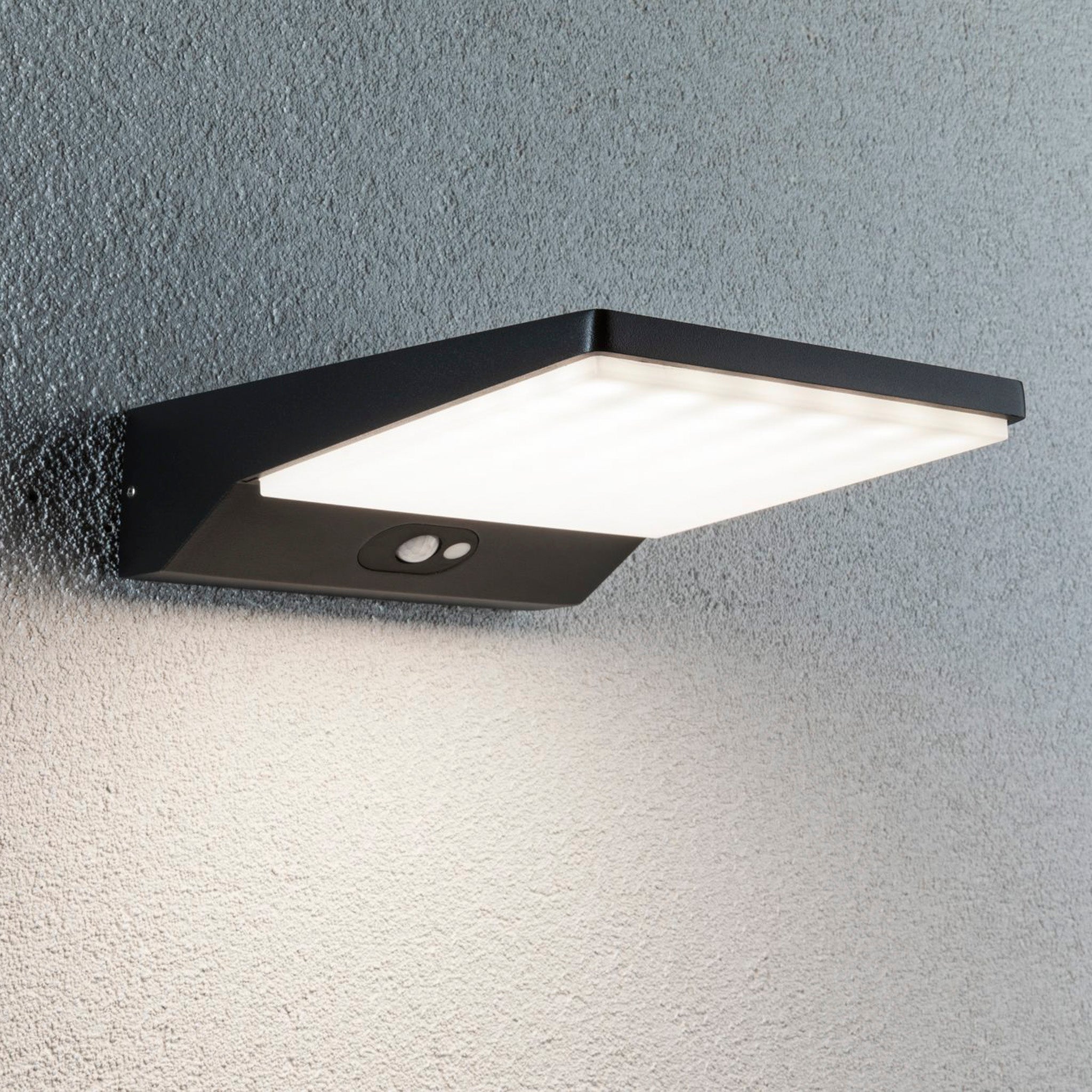 A contemporary, rectangular Paulmann - Outdoor Ronas 5W LED solar wall light with motion detection is tastefully installed on a textured dark grey wall.