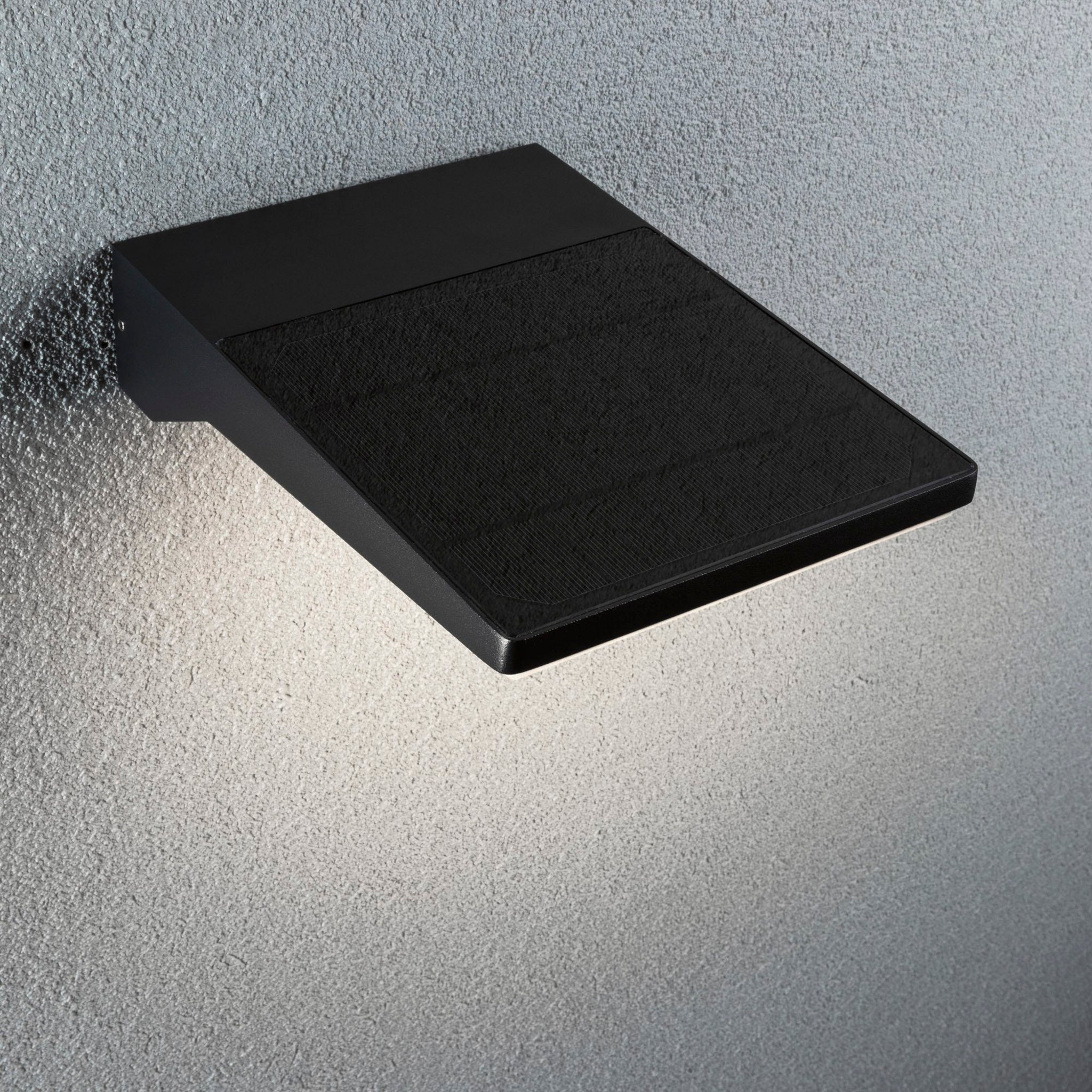 The Outdoor Ronas 5W LED Solar Wall Light with Motion Detection in Dark Grey by Paulmann stylishly lights up a textured gray wall, highlighting the latest advancements in solar technology.