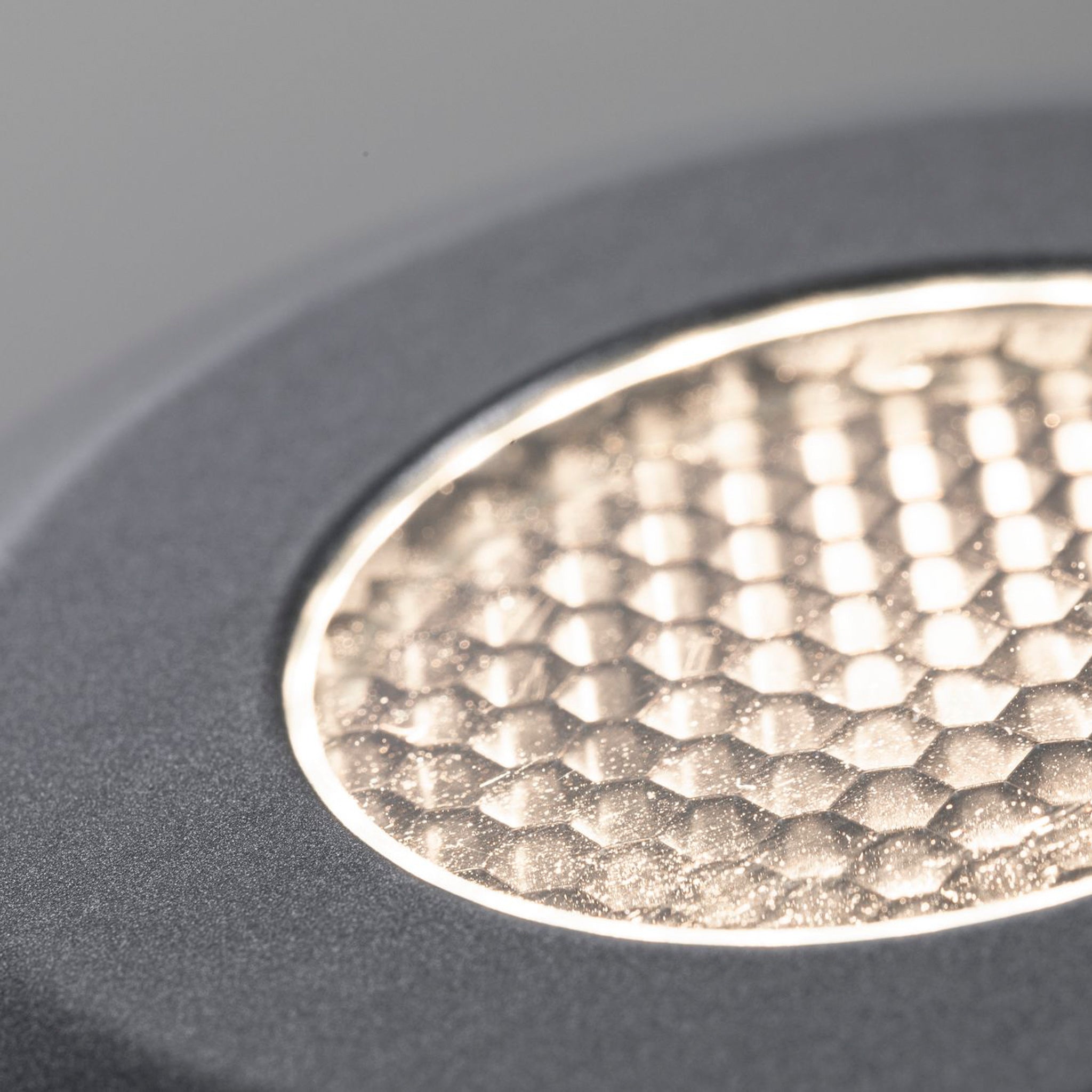 A close-up of a textured, circular light source featuring a honeycomb pattern on a gray background, ideal for enhancing any space. This elegant design seamlessly integrates with the Paulmann - Plug & Shine Outdoor 11W LED Recessed Floor 8.2cm Spotlight in Grey, offering compatibility within the versatile 24-volt LED system.