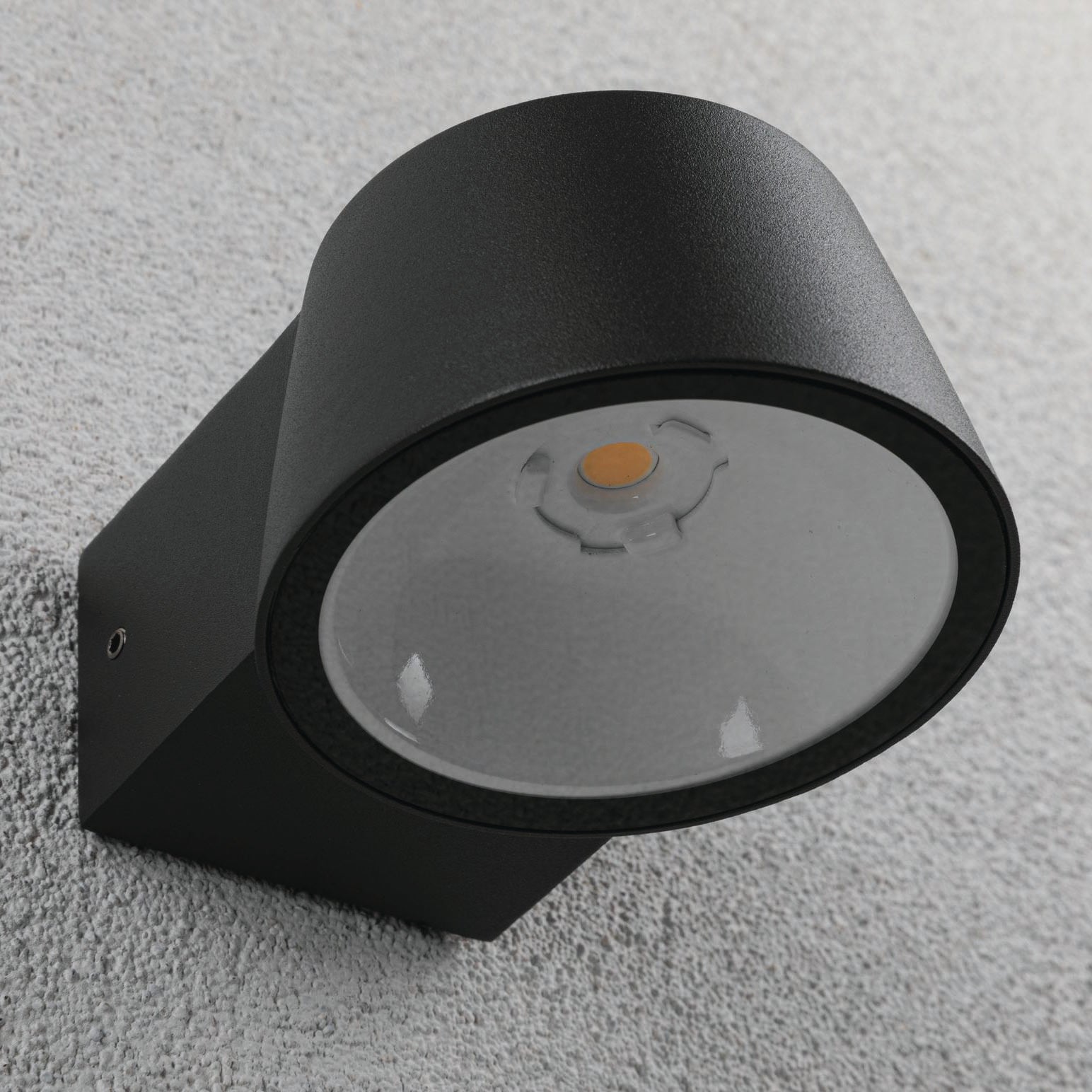 The Paulmann Outdoor Capea 8W LED Wall Light in anthracite features a circular design and is mounted on a textured gray exterior wall, offering an IP44 rating for durability.