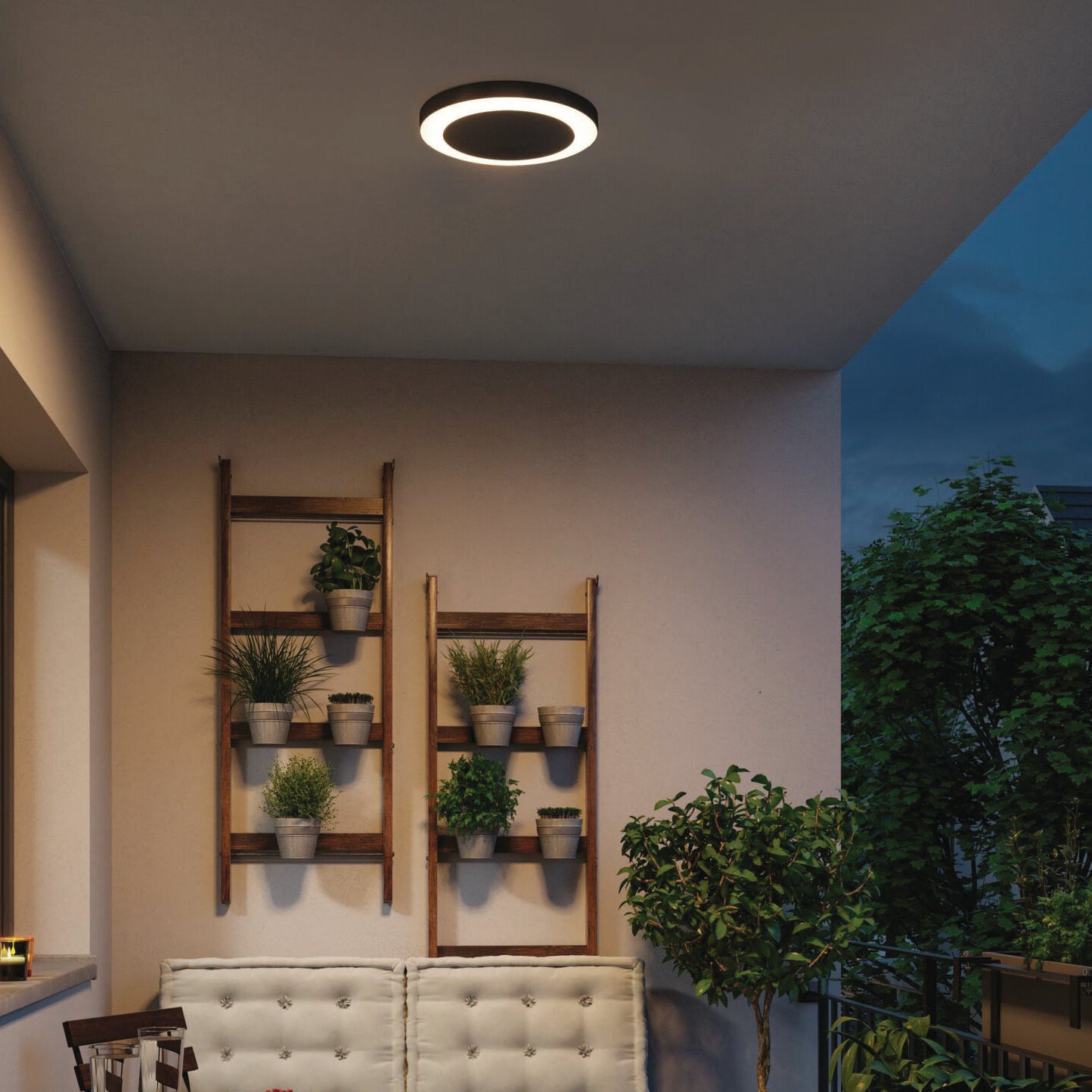 Modern patio with the Paulmann Outdoor Circula Dusk 15W LED Ceiling Light in Anthracite, potted plants on ladder shelves, and cushioned seating enhanced by motion detection for optimal ambiance.