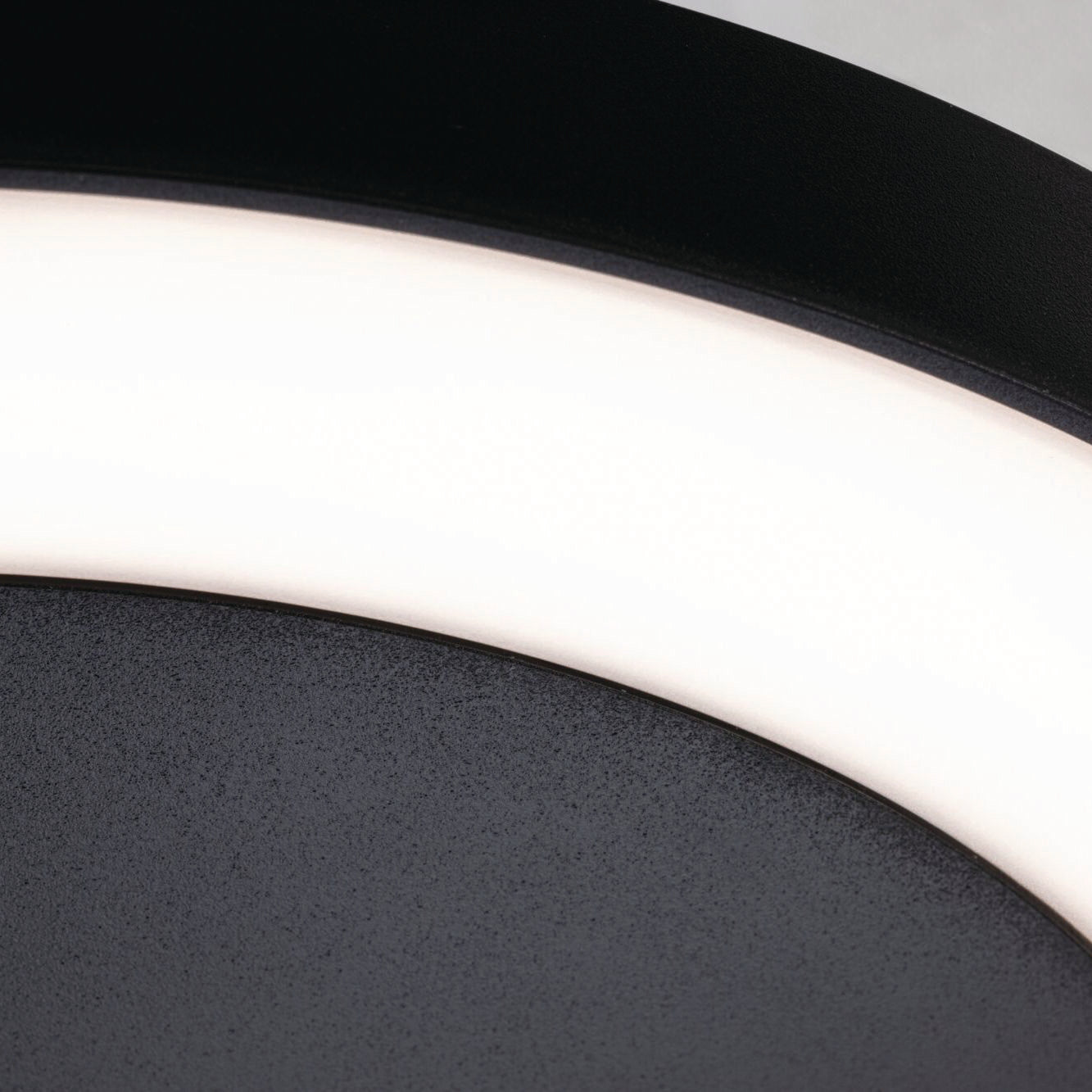 Close-up of a curved, illuminated LED strip from the Paulmann Outdoor Circula Dusk 15W LED Ceiling Light with Motion Detection in Anthracite against a textured black surface.