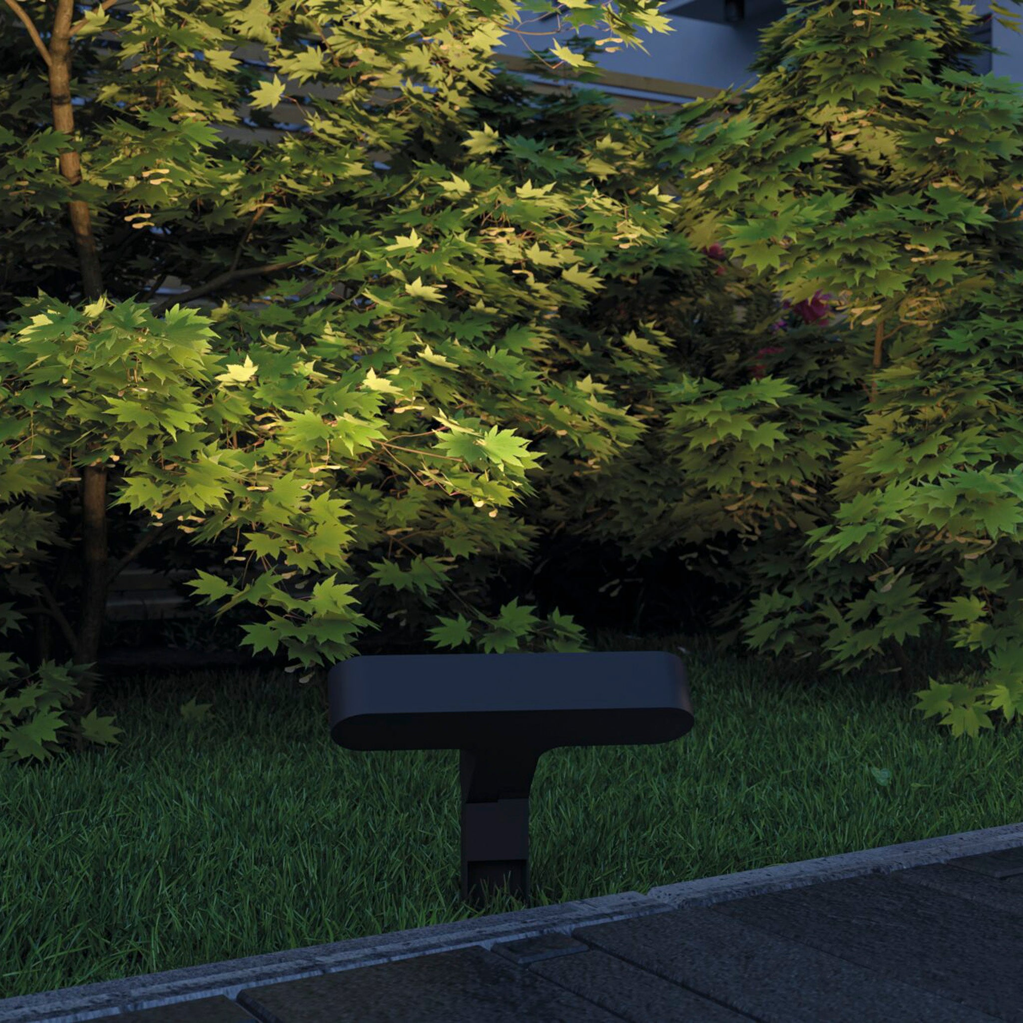 The compact Paulmann Plug & Shine Outdoor Ito 6W LED Horizontal Garden Spotlight in anthracite is nestled among the lush green bushes, casting enchanting outdoor lighting with its asymmetrical beam angle.