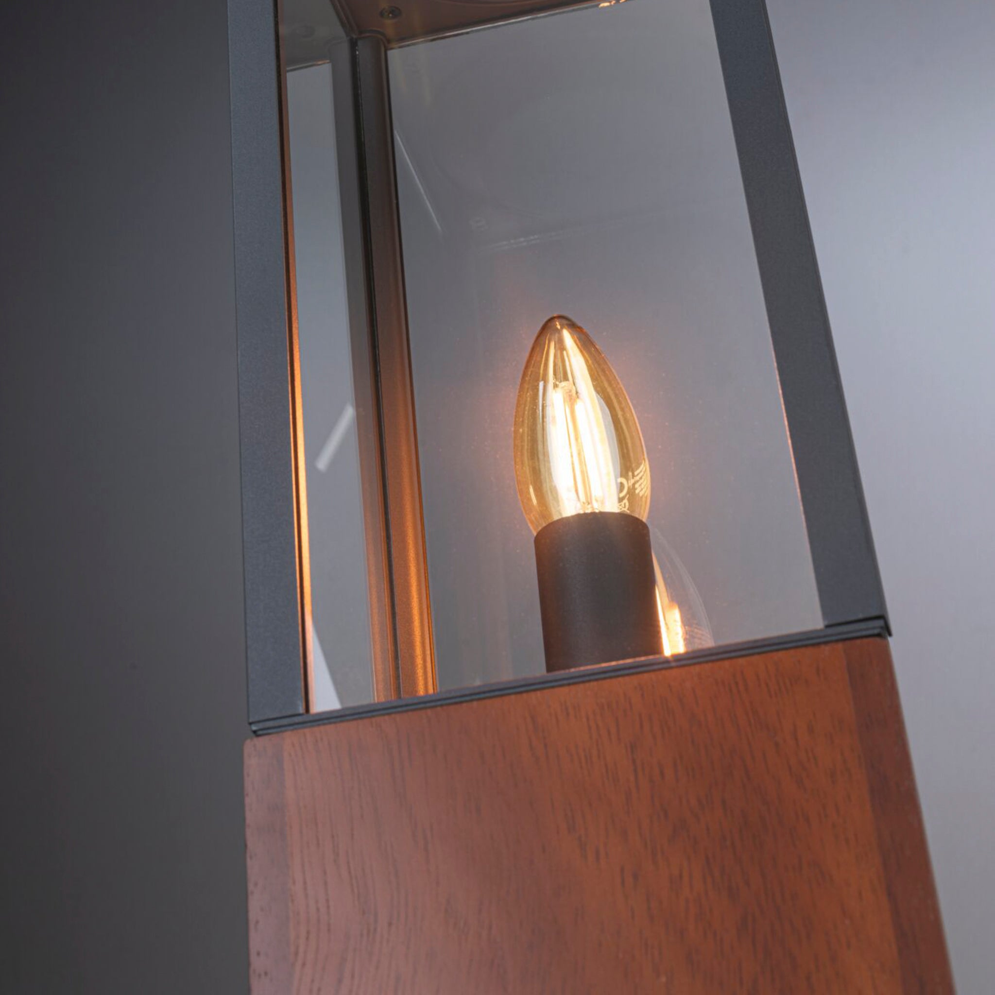 Close-up of the Paulmann - Plug & Shine Outdoor Vena 2W LED 40cm Wooden Single Bollard Light, showcasing its illuminated bulb inside a modern lantern with a wooden base and glass panels, providing atmospheric lighting ideal for outdoor settings.