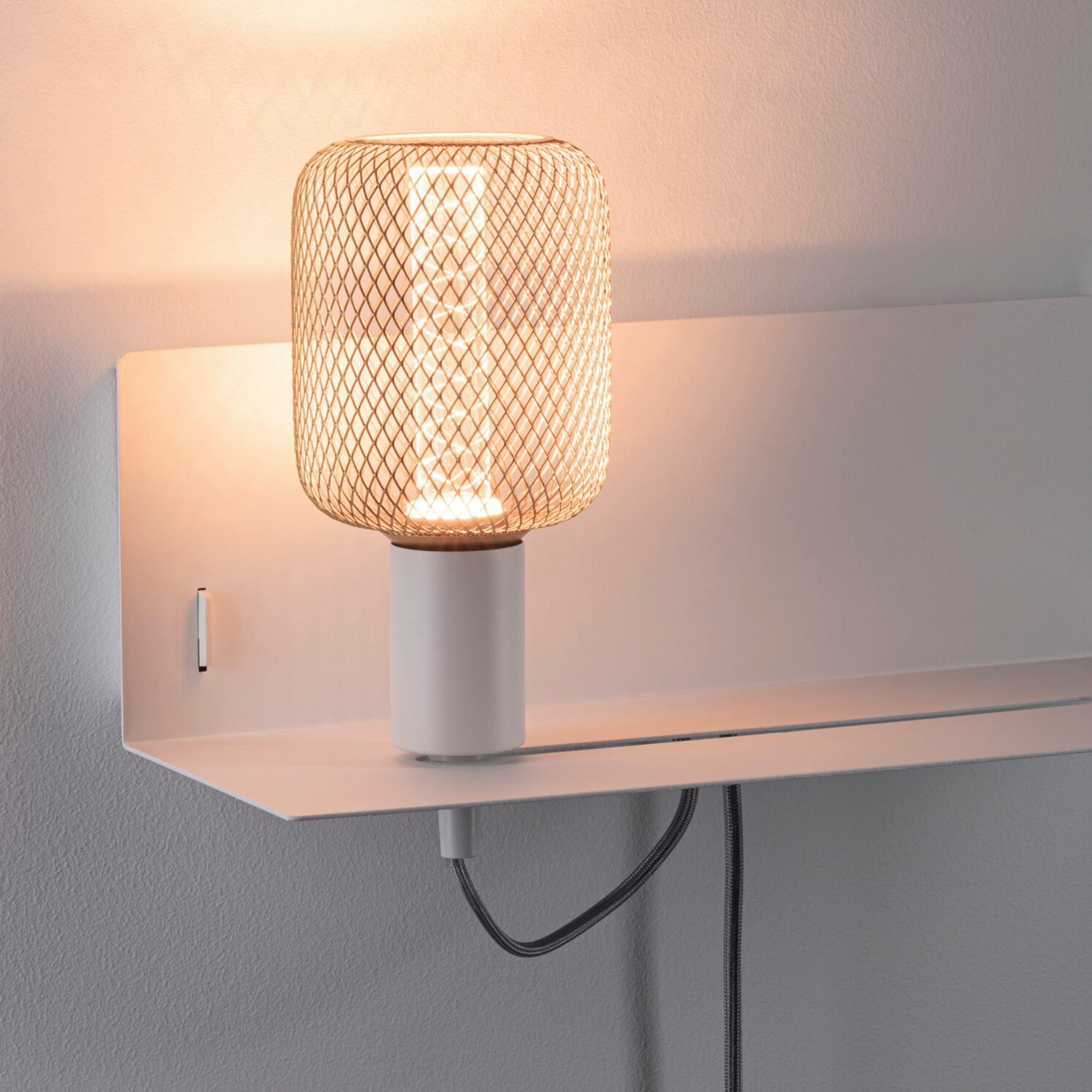 The Devara 40W Wall Mounted Lamp with a mesh shade, integrated shelf, and USB port in White Matt emits a warm light.