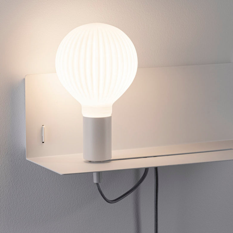 The Devara 40W Wall Mounted Lamp with USB Port in White Matt is a modern wall-mounted reading luminaire featuring a ribbed, globe-shaped light bulb, an integrated shelf, and a visible power cord.